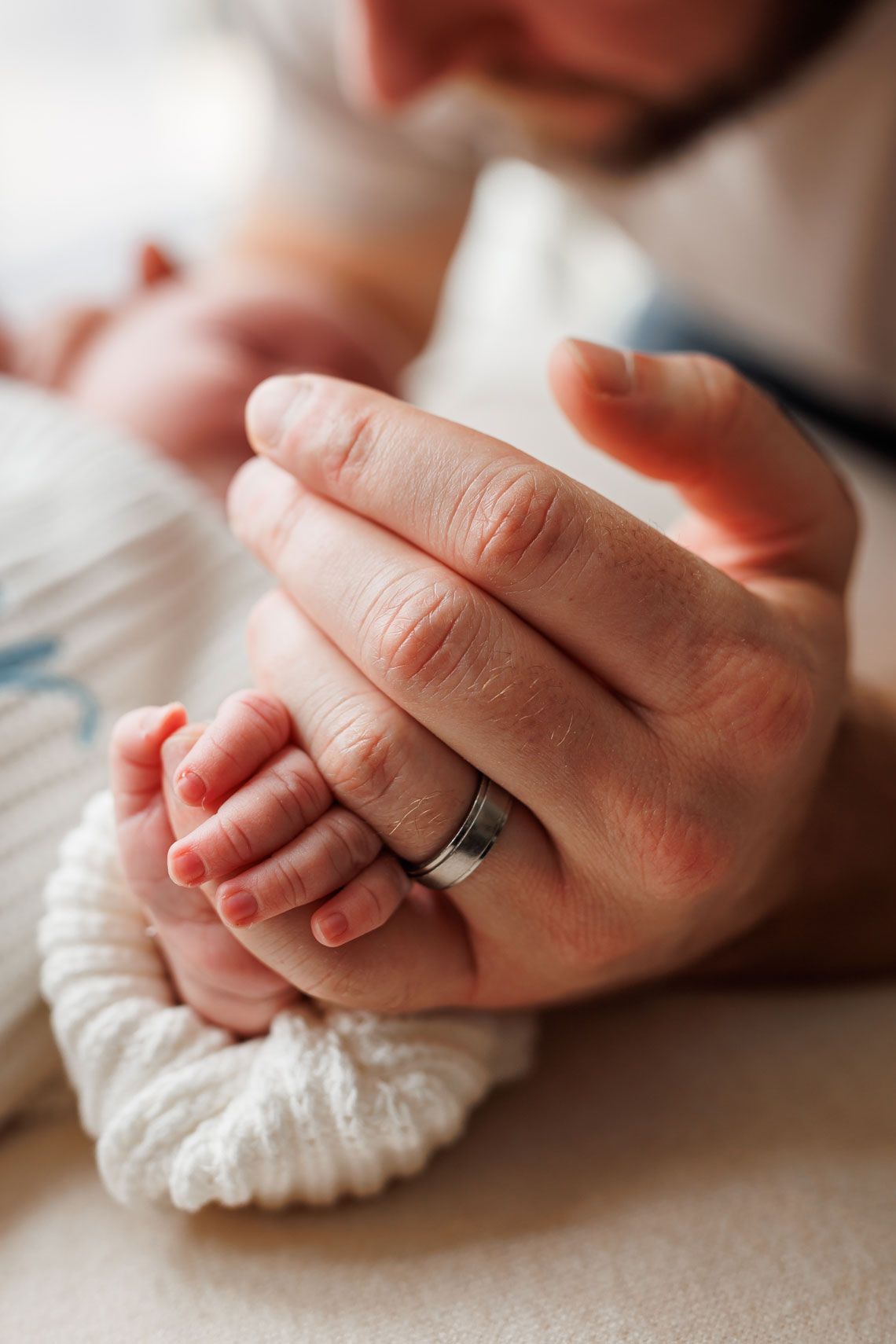 A parent's hand with a wedding ring gently holds a newborn baby's tiny fingers, symbolizing love and new parenthood.