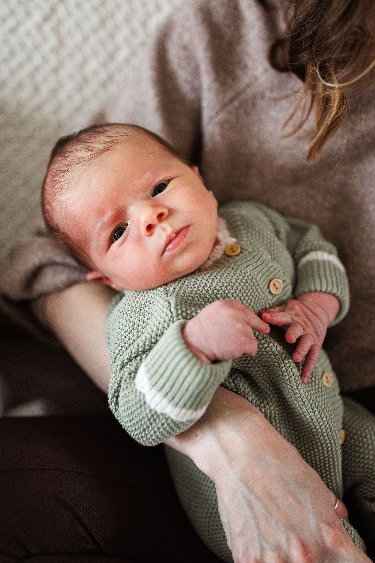 Alert newborn baby in green knit outfit cradled in mother's arms.