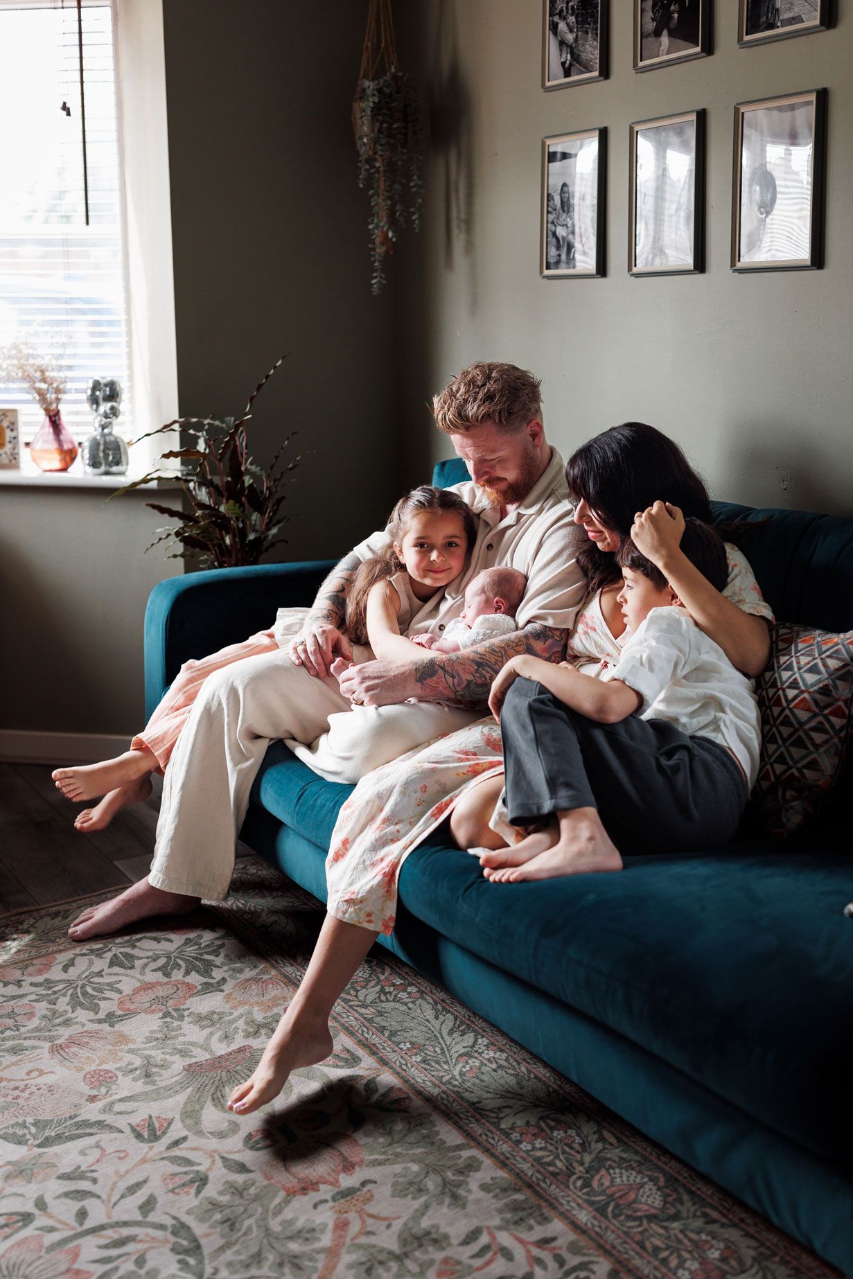 Family of five cuddling together with newborn on a teal sofa in a cozy living room.