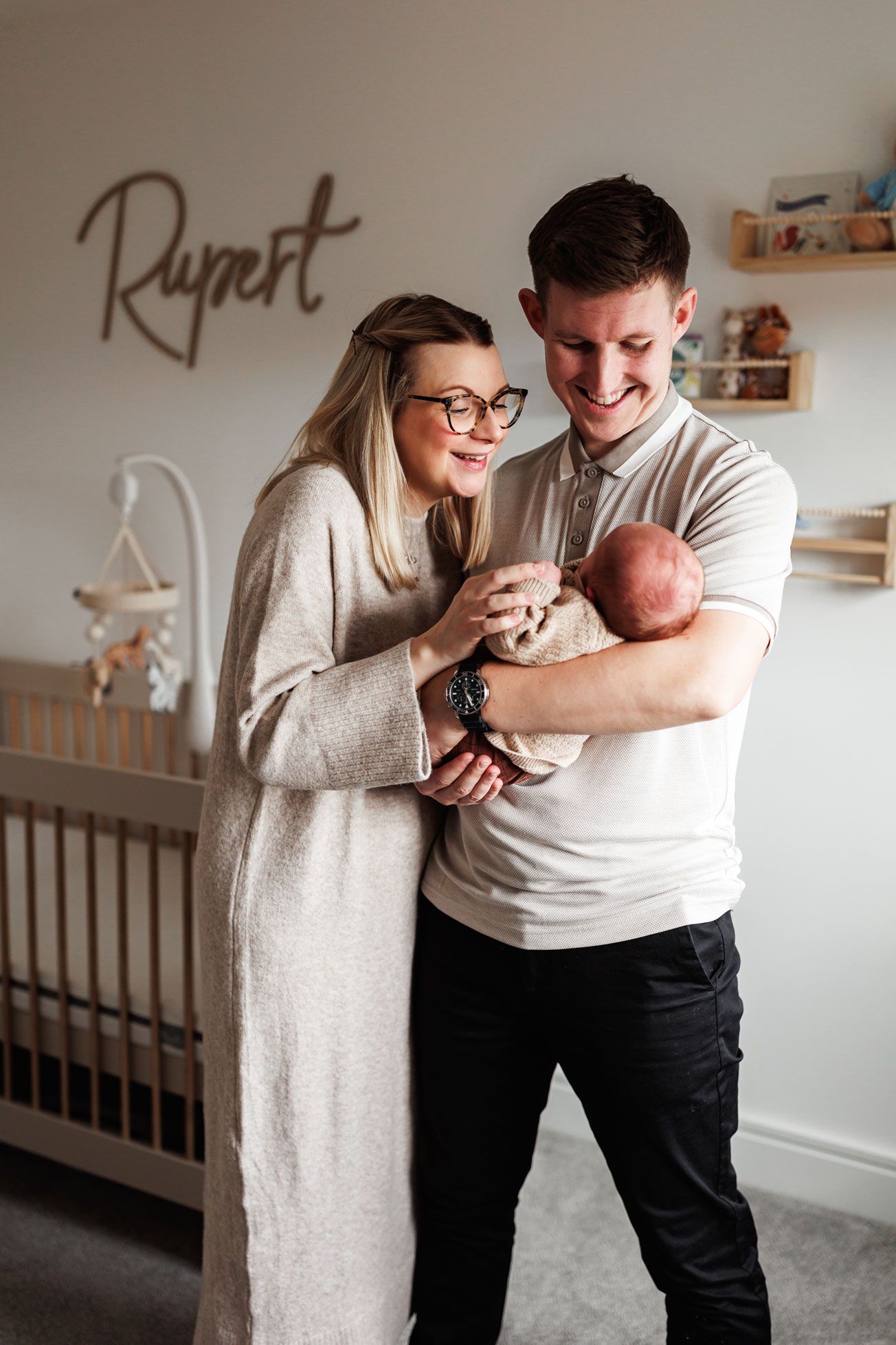 Personalised nursery name sign photographed as part of an at-home newborn photography session, with family moments softly blurred in the bac