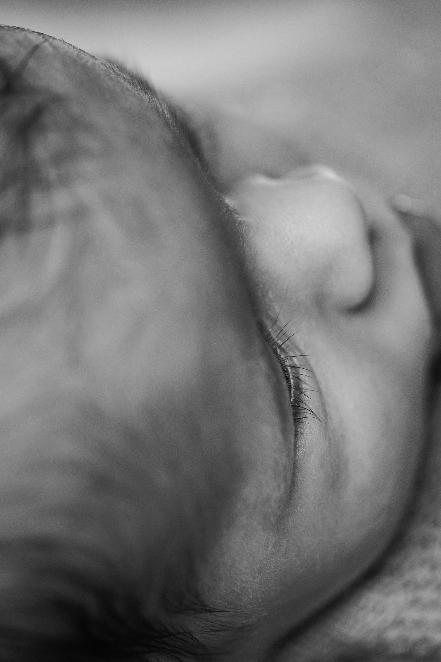 Black and white close-up portrait of a sleeping newborn baby showing delicate eyelashes and features.