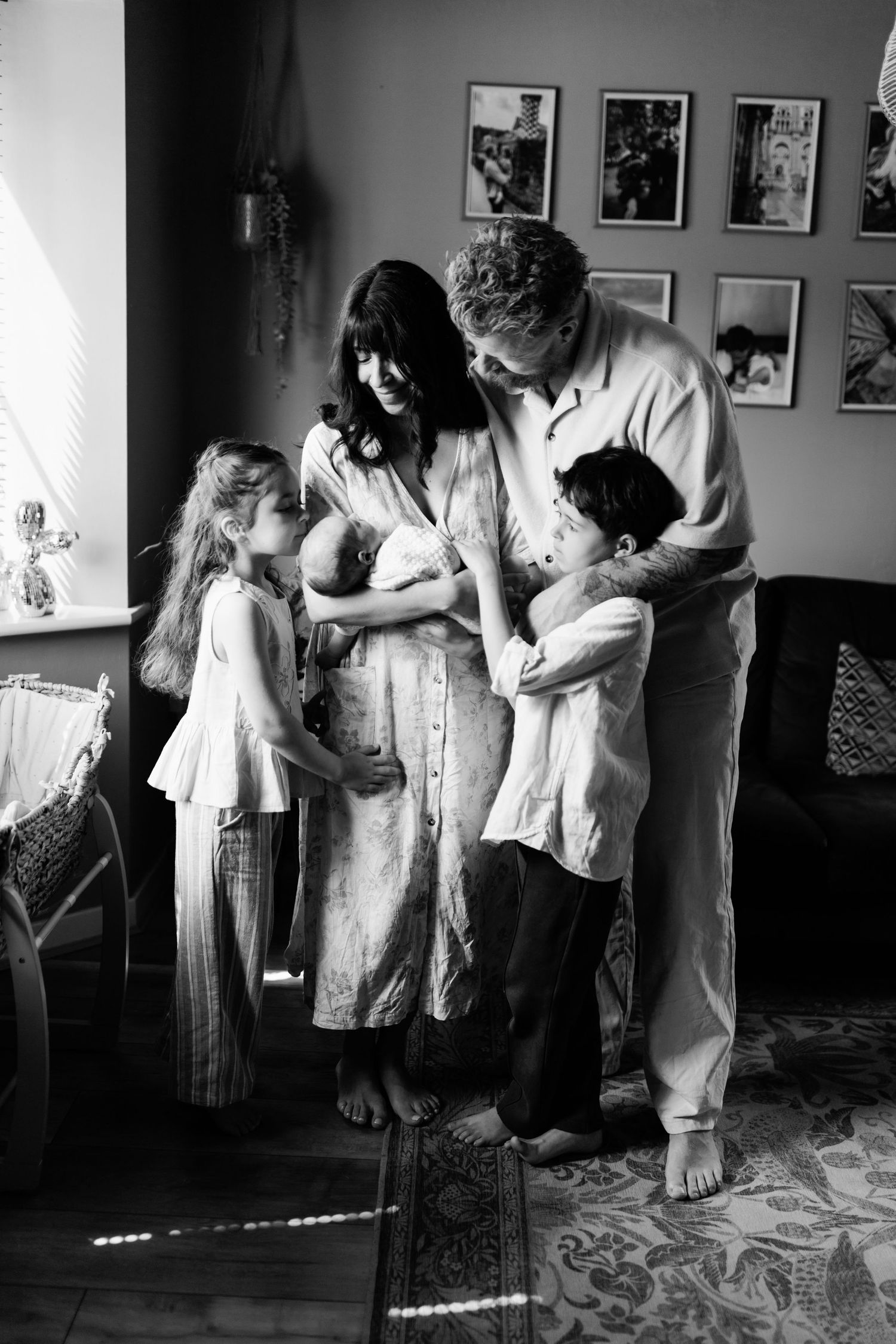 Black and white photo of family of five gathered around mother holding newborn baby indoors.