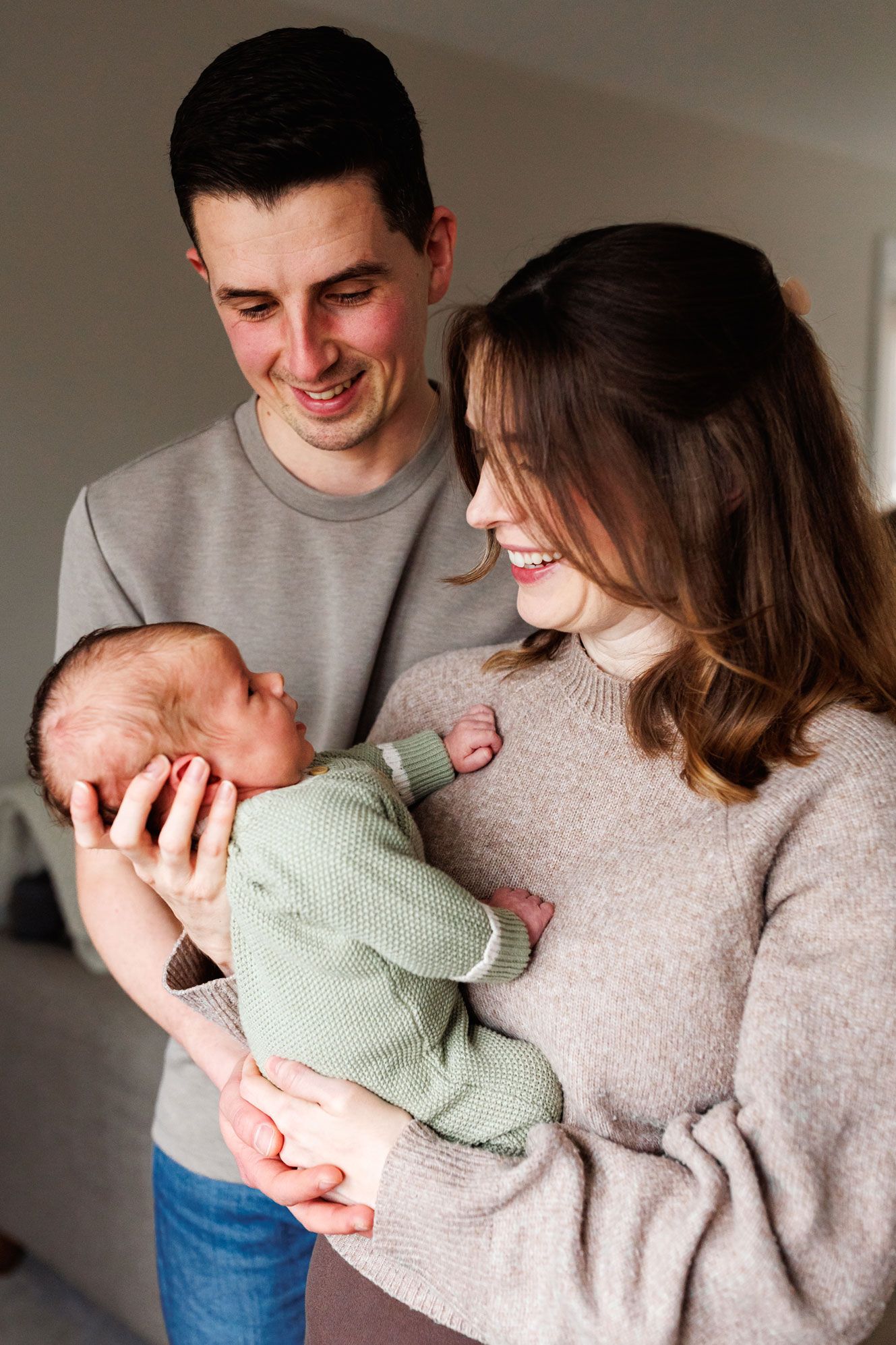 Happy parents smiling at their newborn baby in green knit outfit.