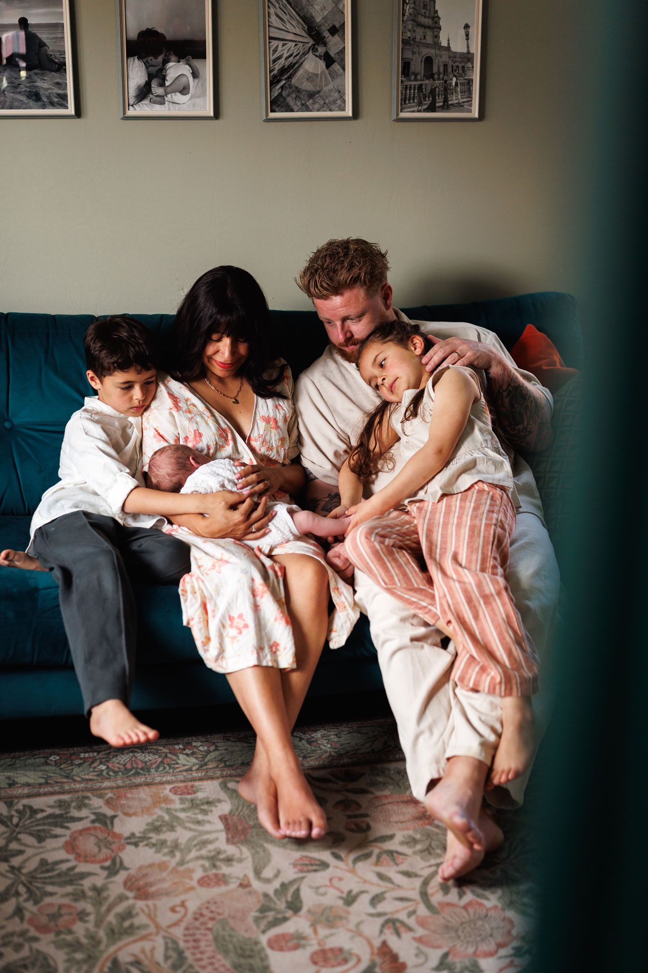 Family of five with newborn baby snuggled together on a teal couch at home.
