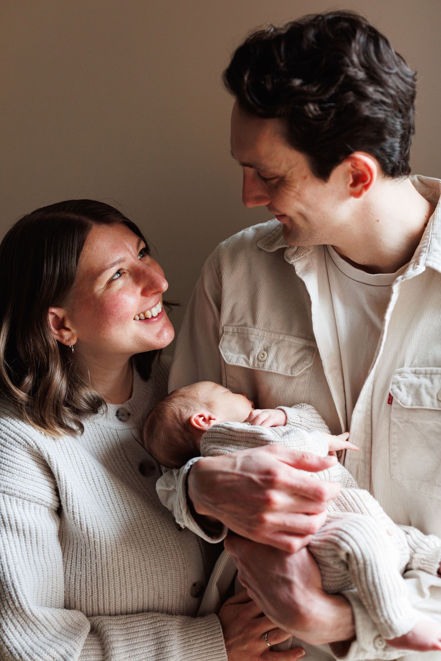 Smiling new parents holding their newborn baby together, sharing a joyful moment in soft neutral tones.