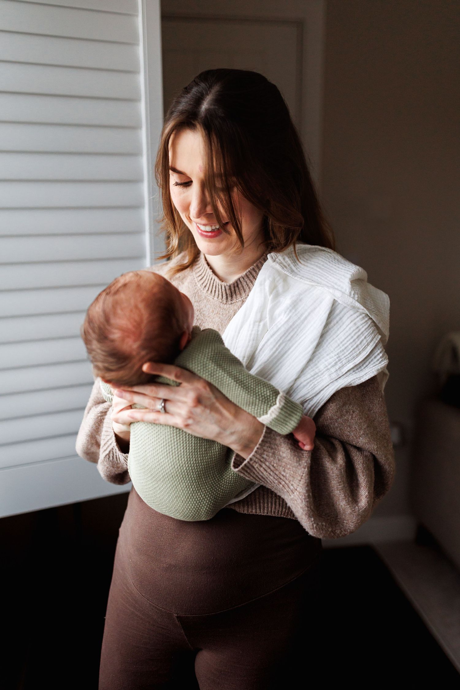 Smiling mother gazing lovingly at her newborn baby near a window.