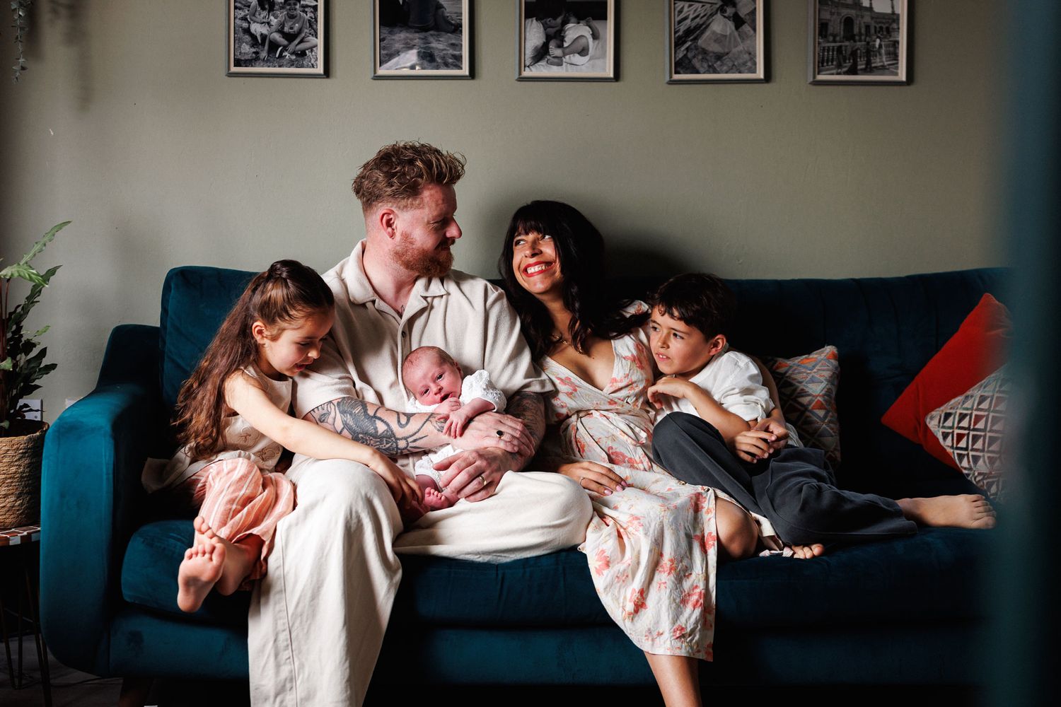 Happy family of five with newborn baby relaxing on a teal sofa in a cozy home.