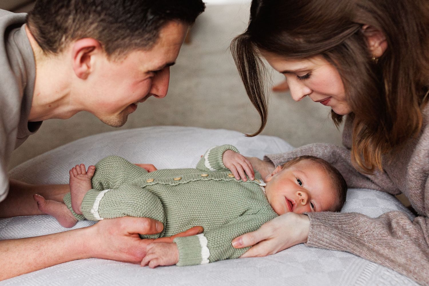 Loving parents leaning over their newborn baby in a green knit outfit.