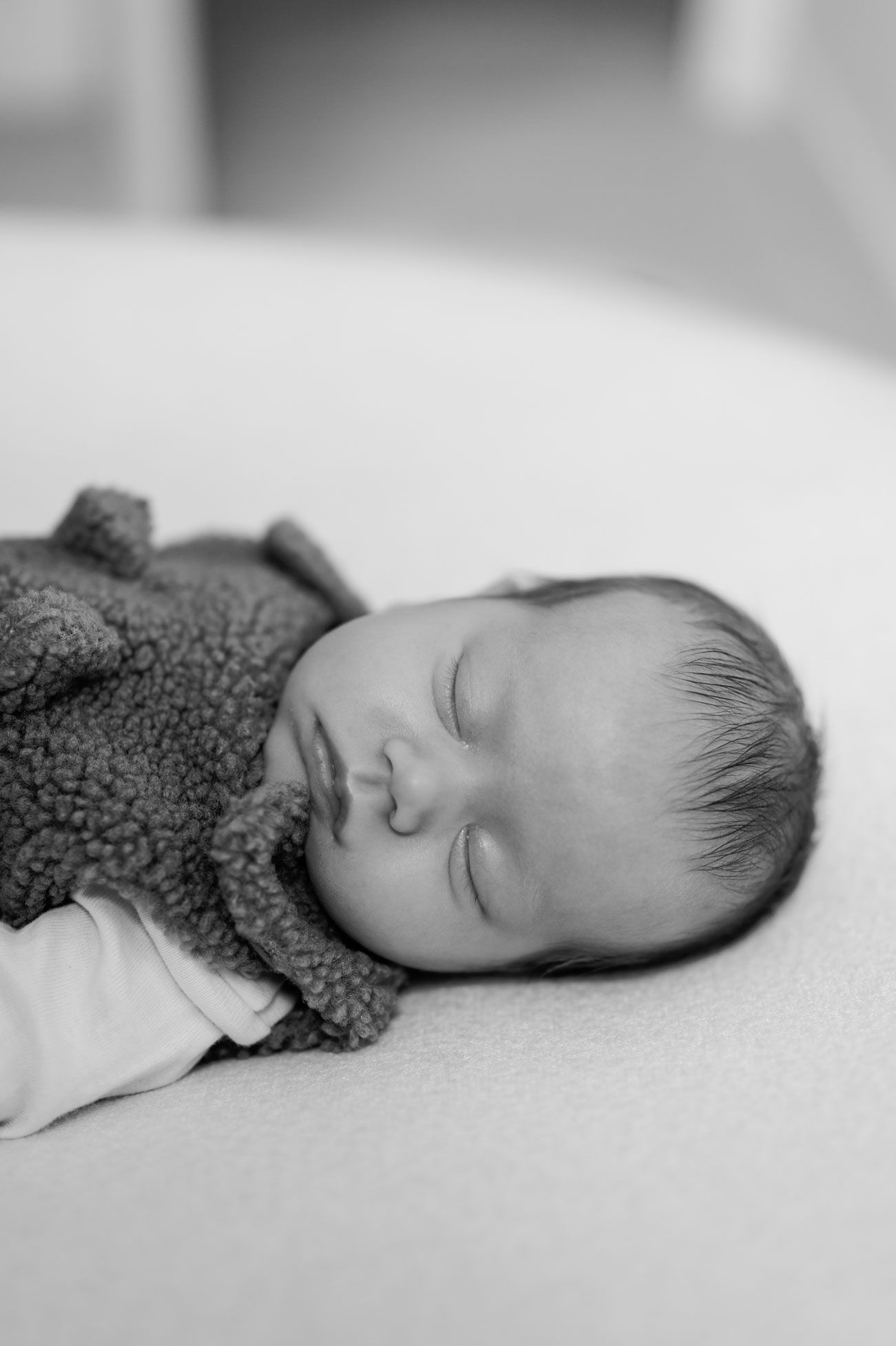 Black and white photo of a sleeping newborn baby in a fuzzy sherpa vest, lying peacefully on a soft blanket.