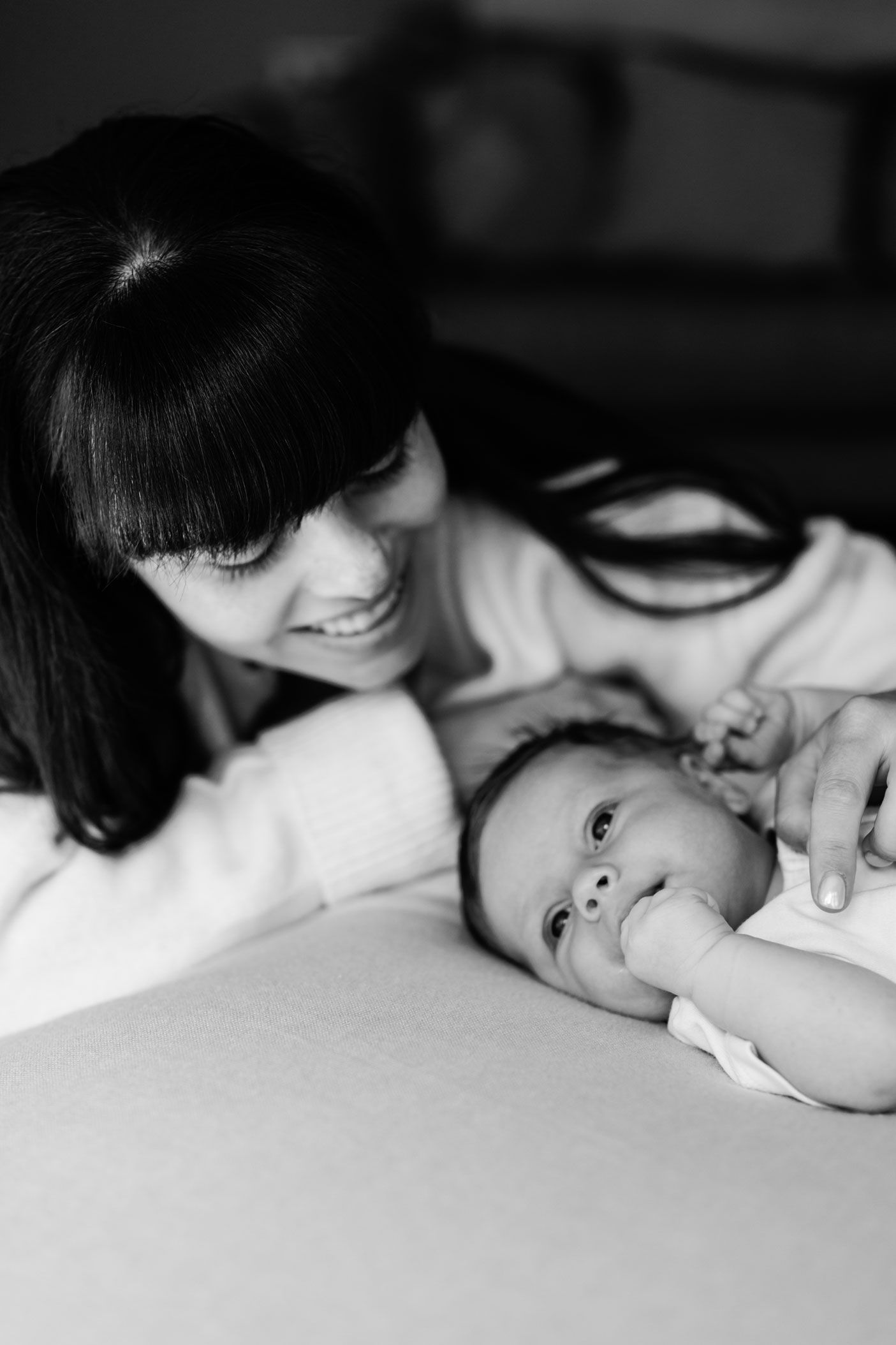Black and white photo of a smiling mother leaning over her newborn baby lying on a soft surface.