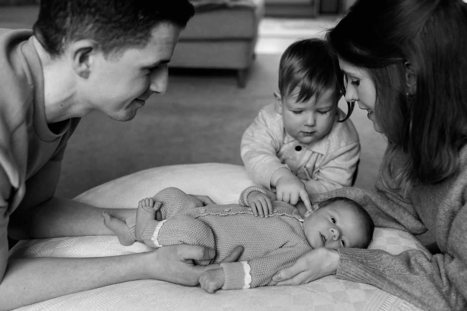 Black and white photo of parents and toddler meeting their newborn baby.