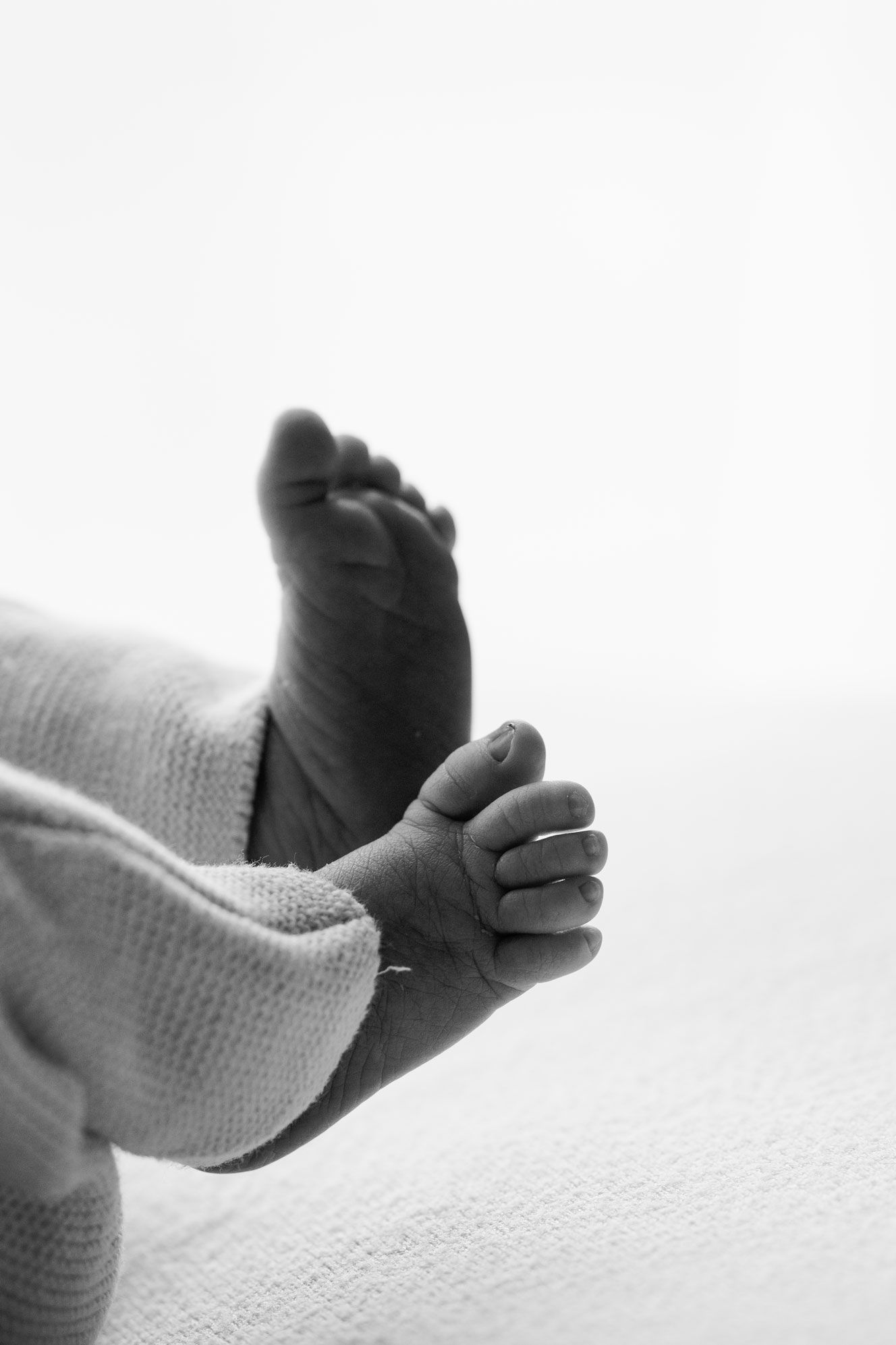 Black and white close-up of a newborn baby's tiny foot and curled hand resting on a soft knit blanket.