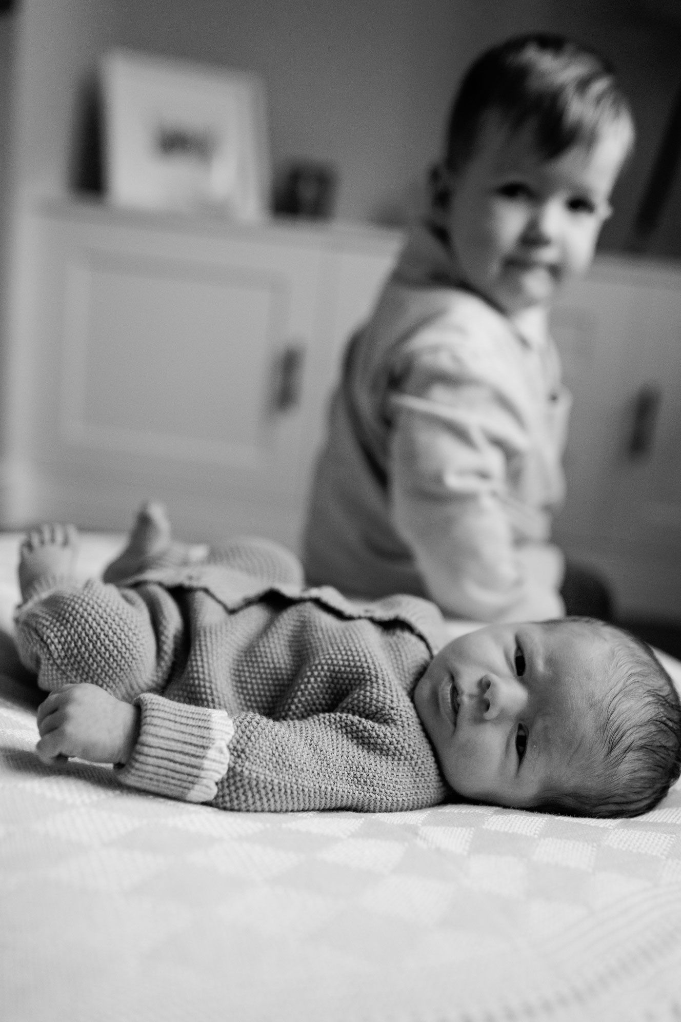 Black and white photo of newborn baby with older toddler sibling.