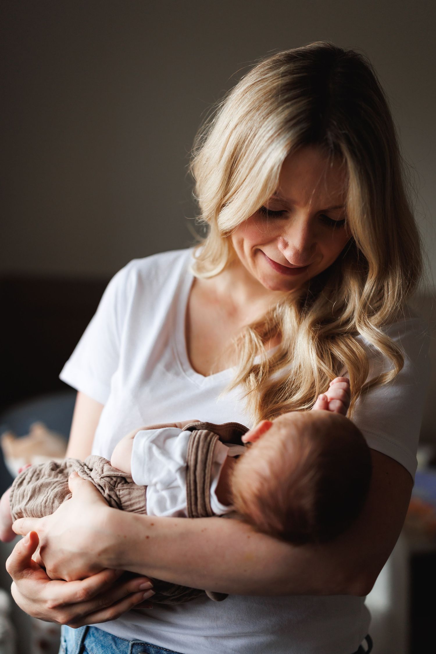 Blonde mother in white t-shirt tenderly cradling her newborn baby in her arms indoors.
