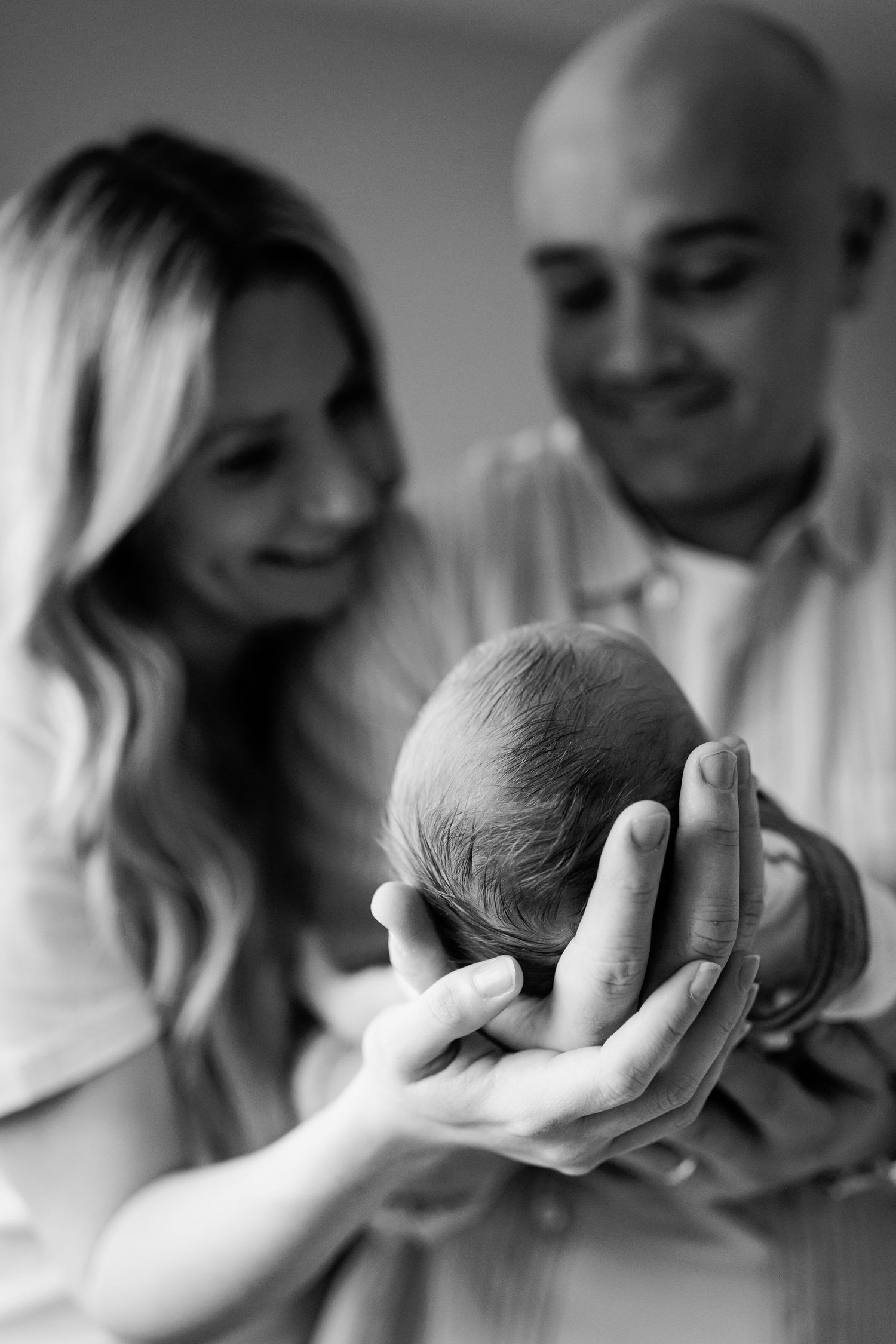 Black and white photo of smiling parents holding their newborn baby's head in focus.