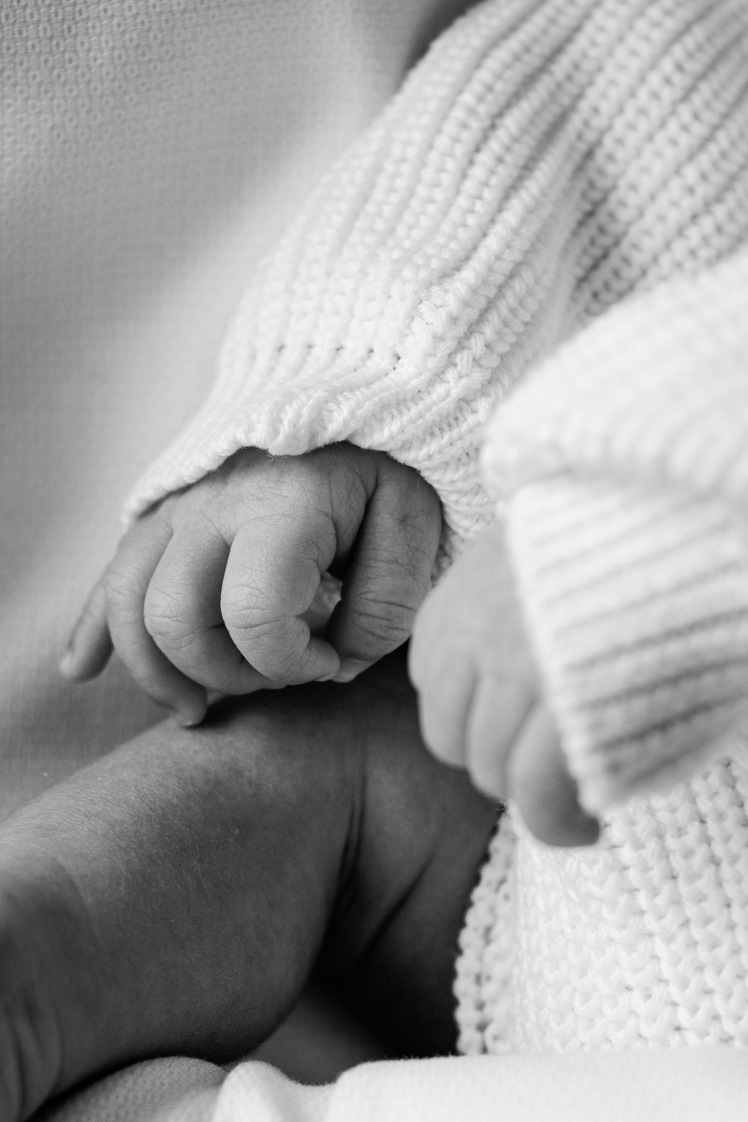 Black and white close-up of a newborn baby's tiny fist in a knit sweater.