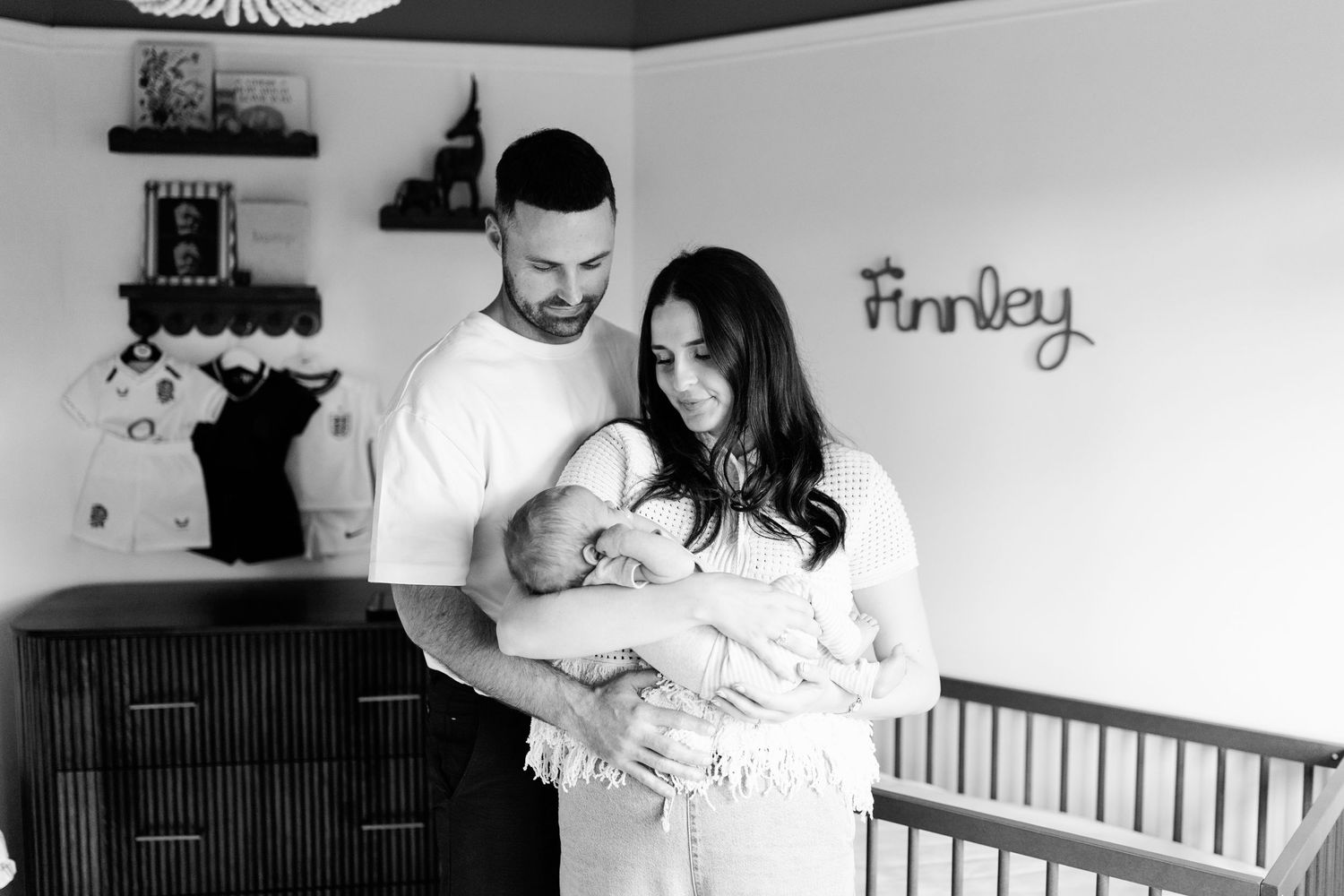 New parents holding their newborn baby in a nursery during a relaxed lifestyle newborn photography session at home.