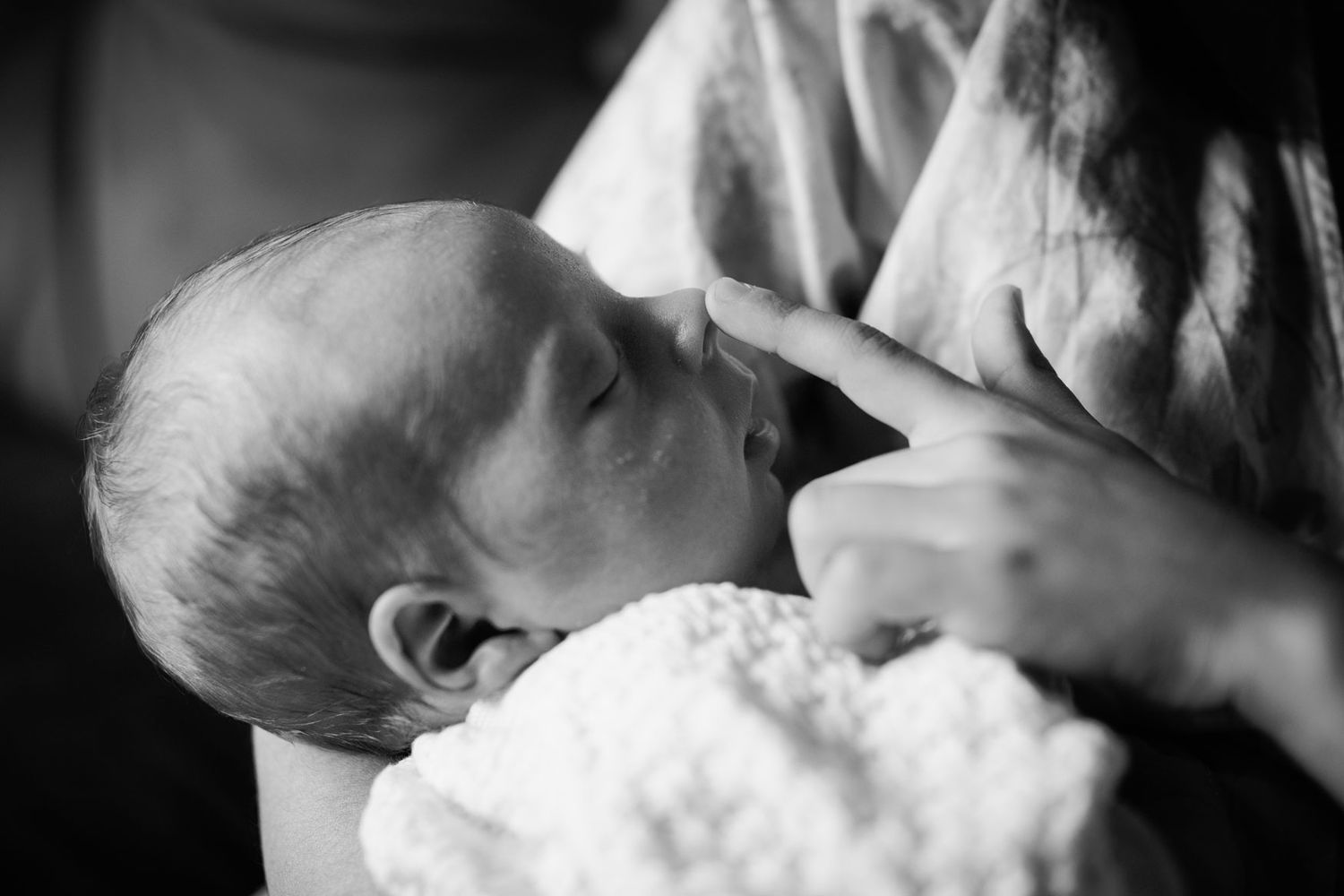 Black and white close-up of a newborn baby being gently touched on the nose.