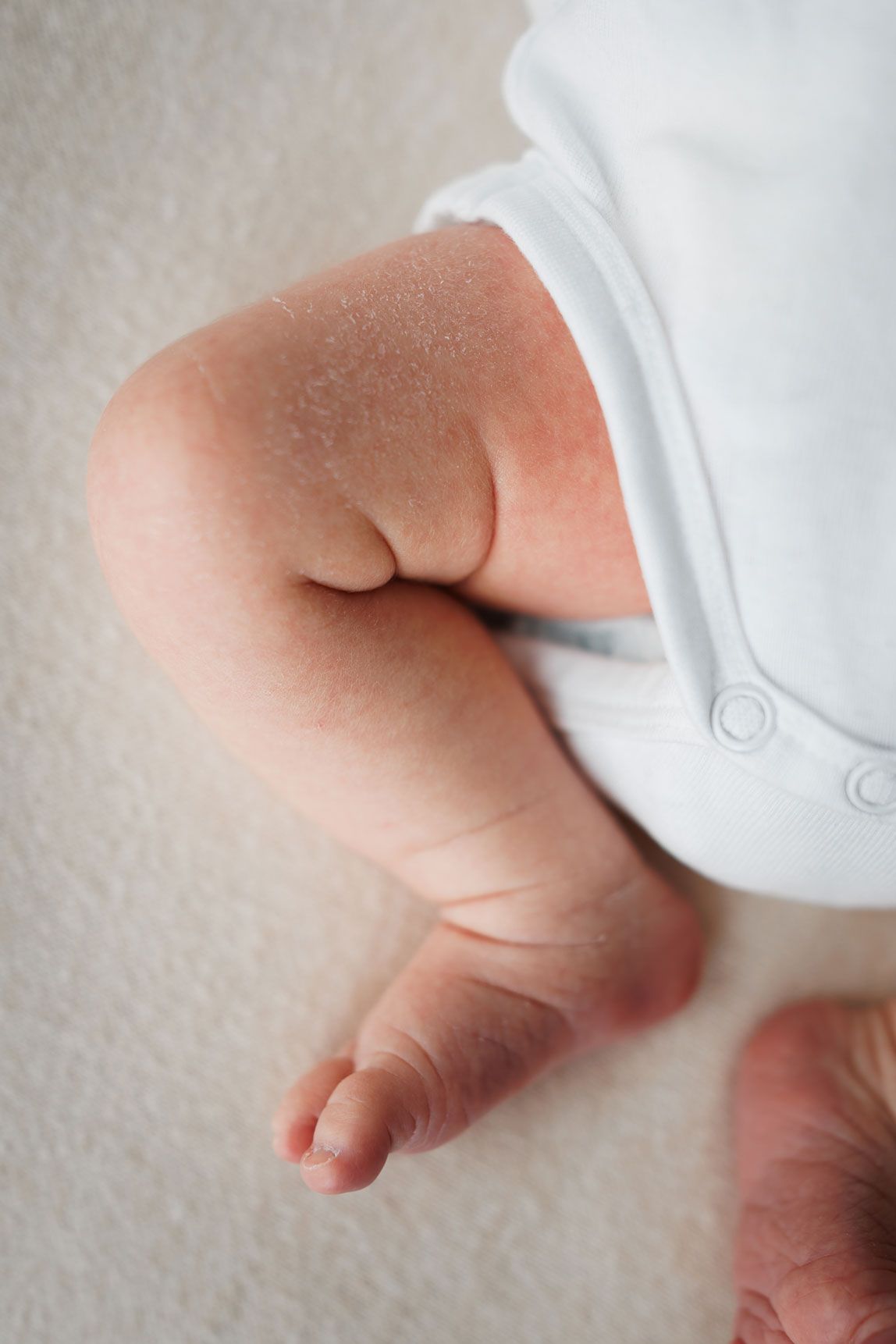 Close-up of newborn baby's chubby legs and tiny feet in a white onesie.
