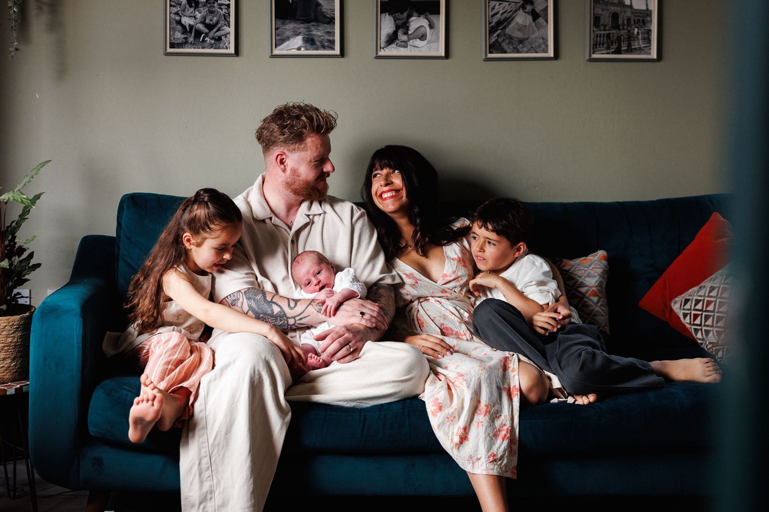 Happy family of five with newborn baby relaxing together on a teal sofa at home.