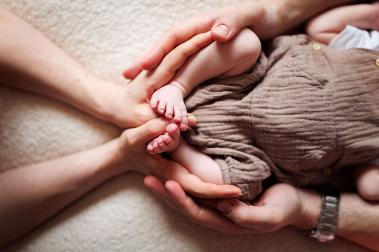 Parents tenderly holding newborn baby feet and hands together on a soft white blanket in Nottingham