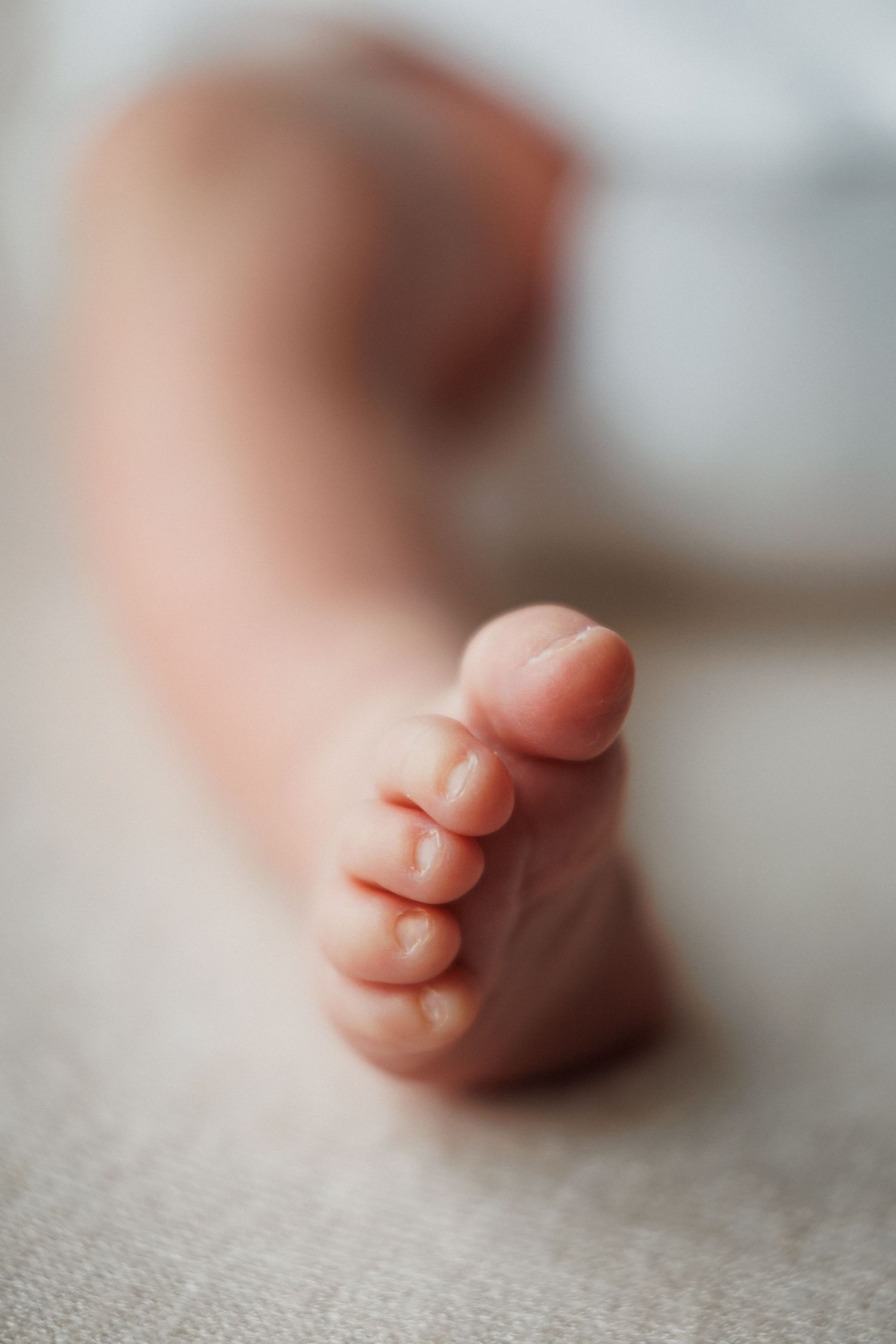 Soft focus close-up of a newborn baby tiny foot resting on a light textured surface.