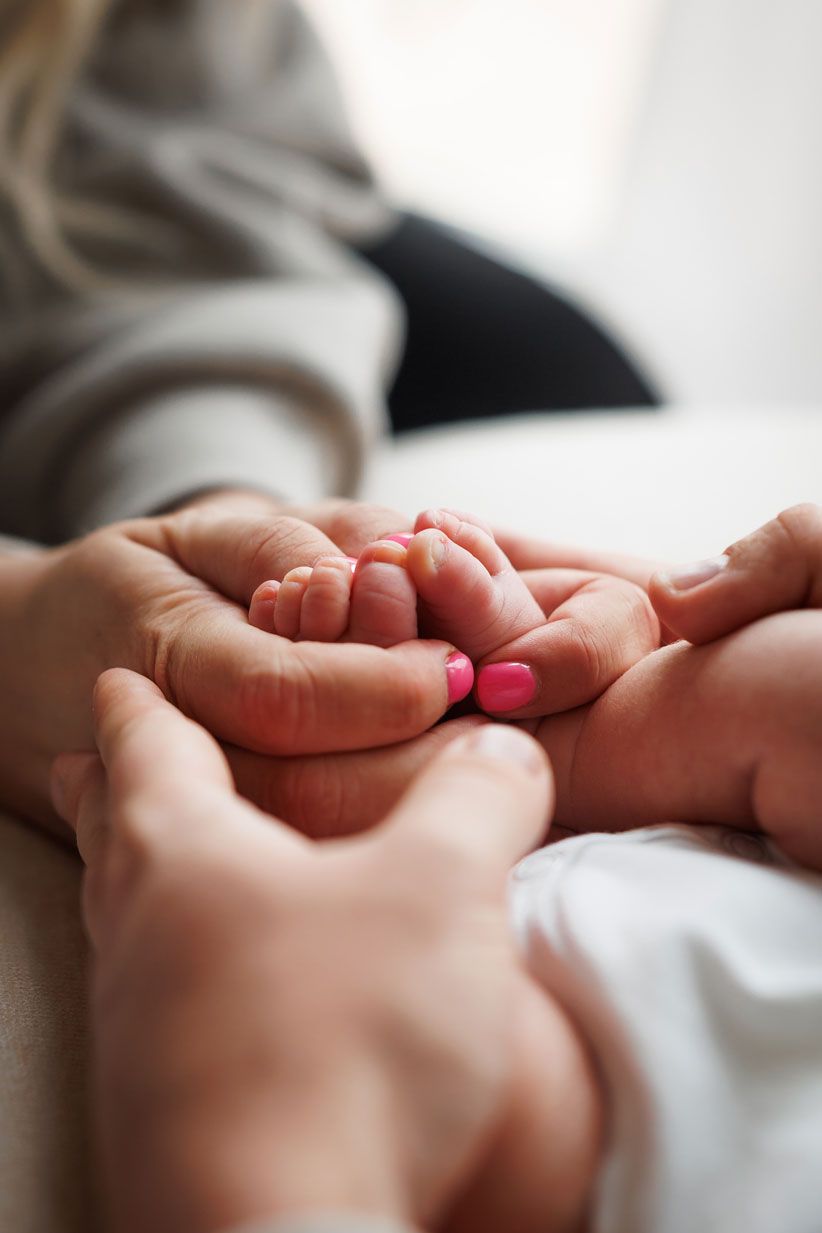 Parents tenderly hold their newborn baby's tiny feet in cupped hands, showing love and care.