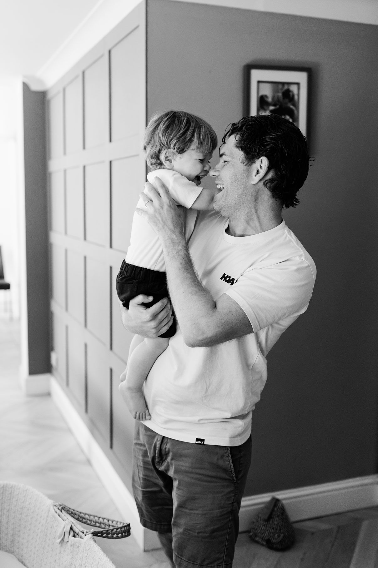 Black and white photo of a smiling man holding a happy toddler up close, sharing a joyful moment indoors.