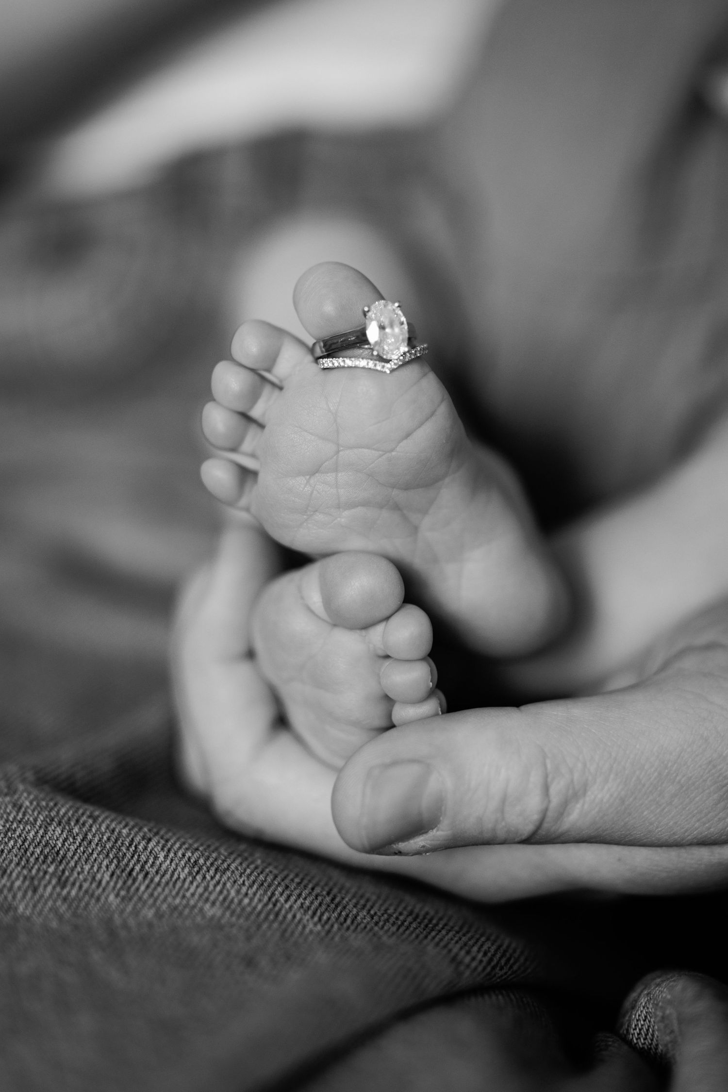 Black and white close-up of a diamond engagement ring placed on a newborn babys tiny foot.