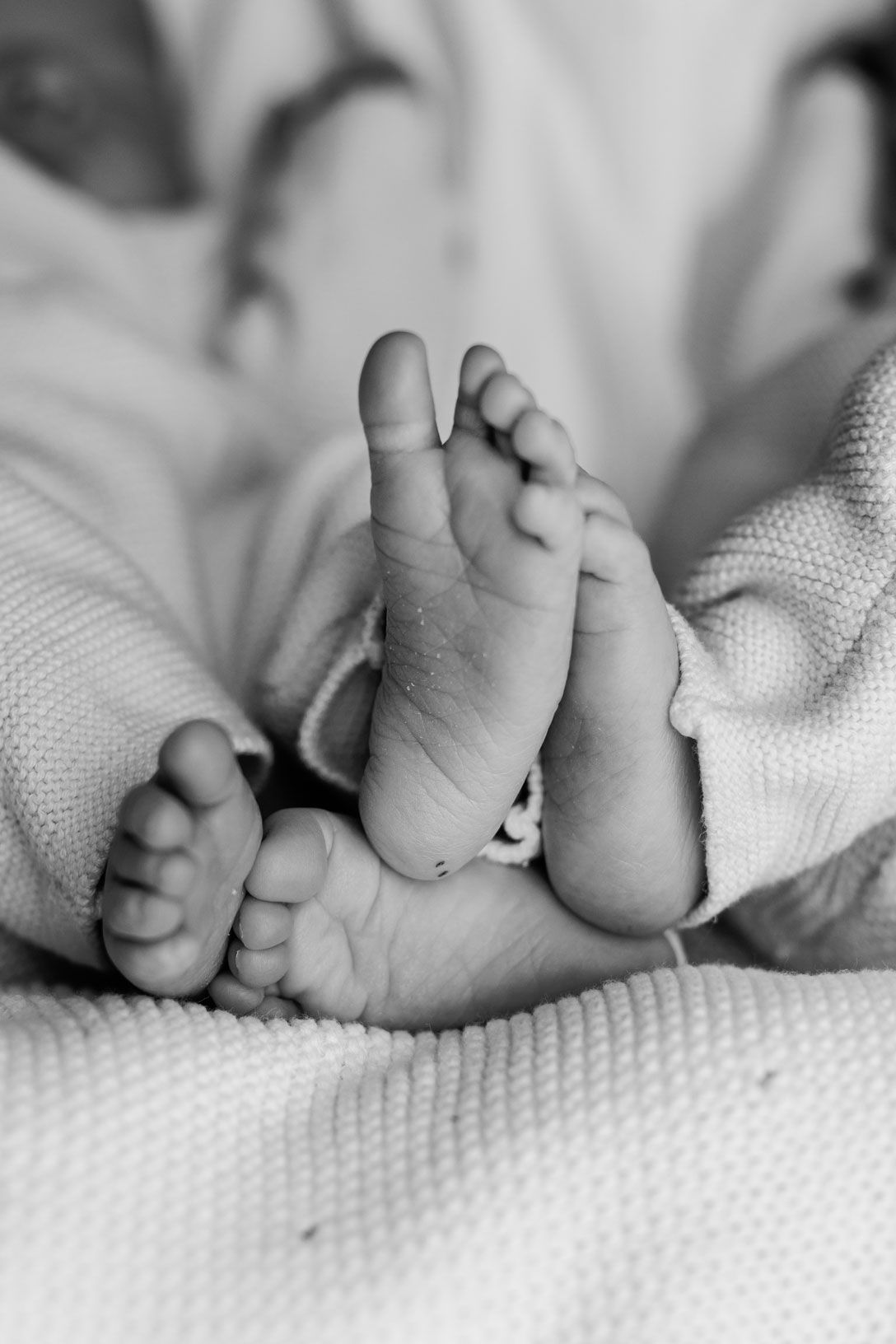 Black and white close-up of a newborn baby's tiny feet resting on a soft knit blanket.