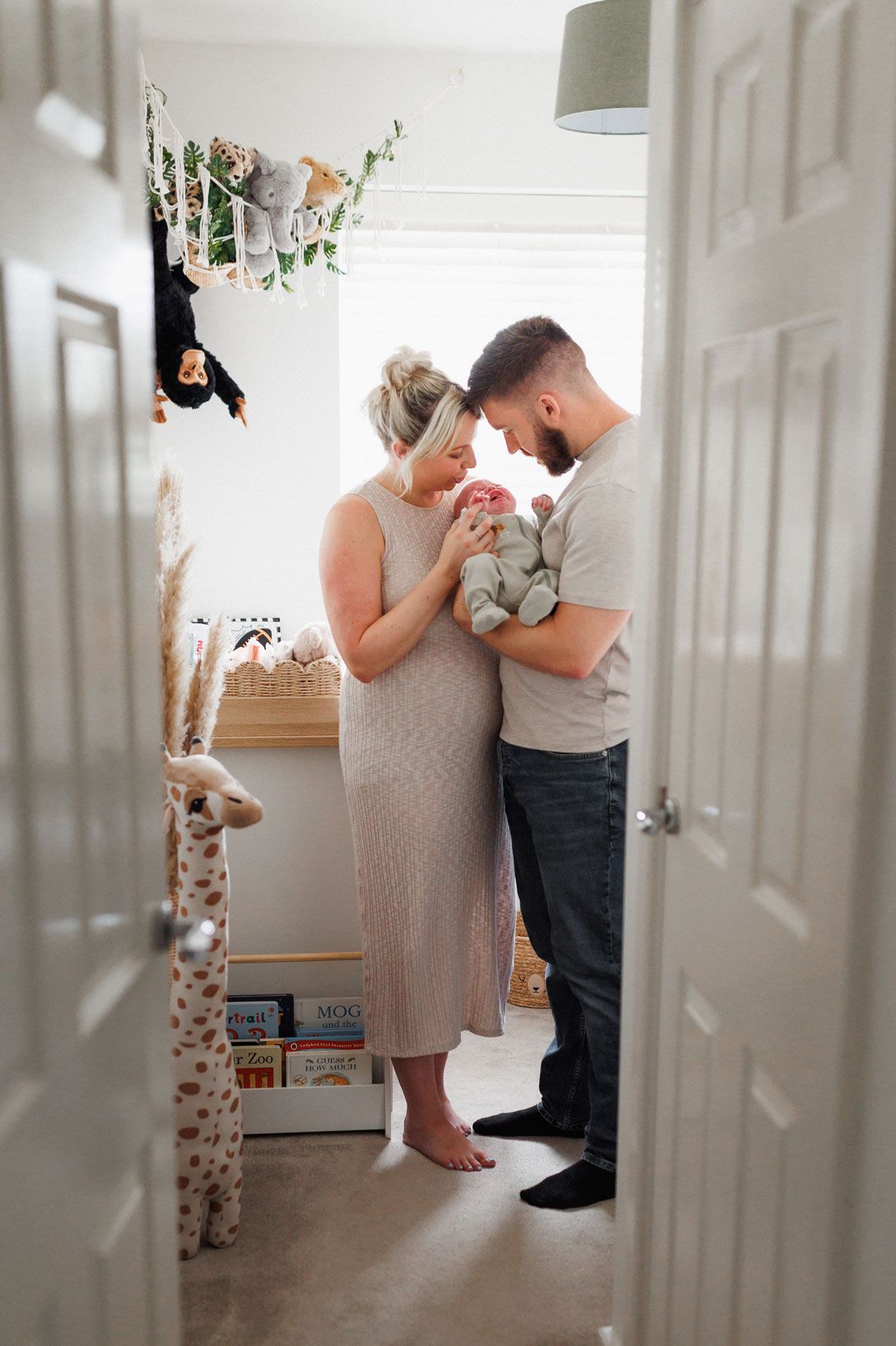 A couple tenderly holds their newborn baby in a cozy nursery filled with stuffed animals and toys.