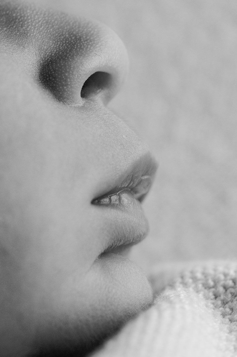 Black and white close-up profile of a sleeping baby's nose and lips resting against a soft knit blanket.