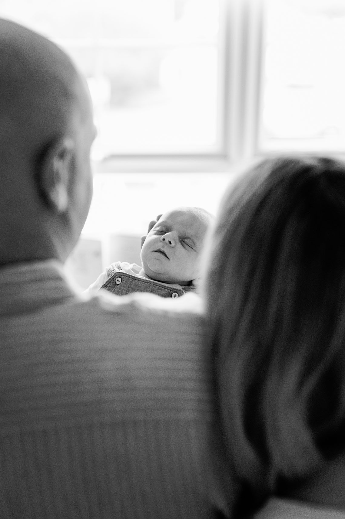 Black and white photo of parents lovingly gazing at their newborn baby near a bright window in their Nottingham Newborn Session