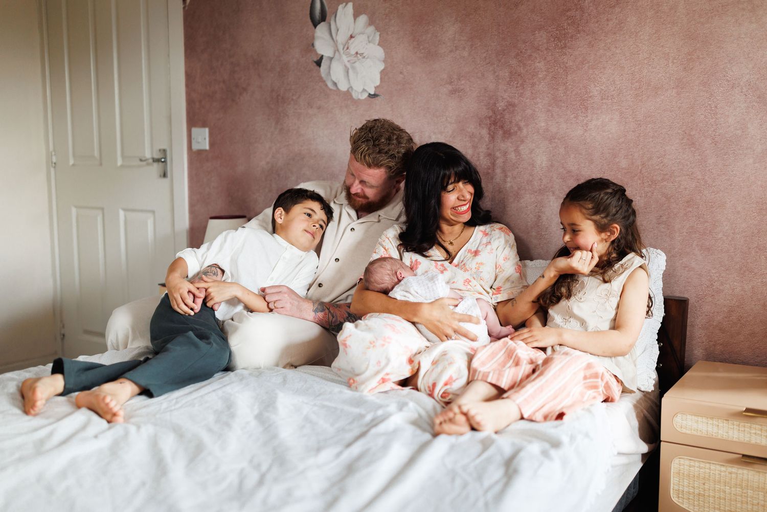 Happy family of five with newborn baby relaxing together on a bed at home.