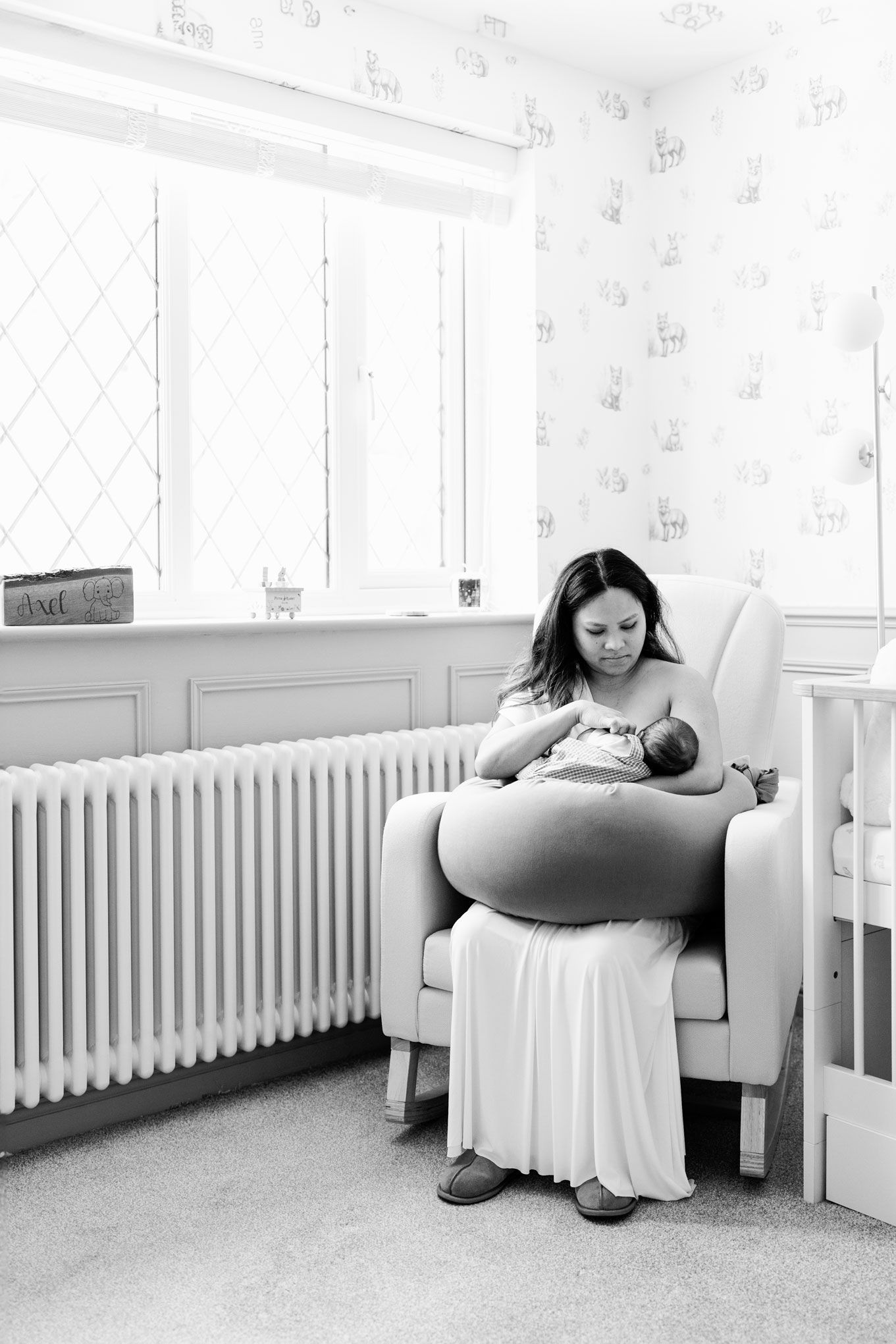 Mother feeding her newborn baby in a nursery chair during a documentary-style at-home newborn photography session.