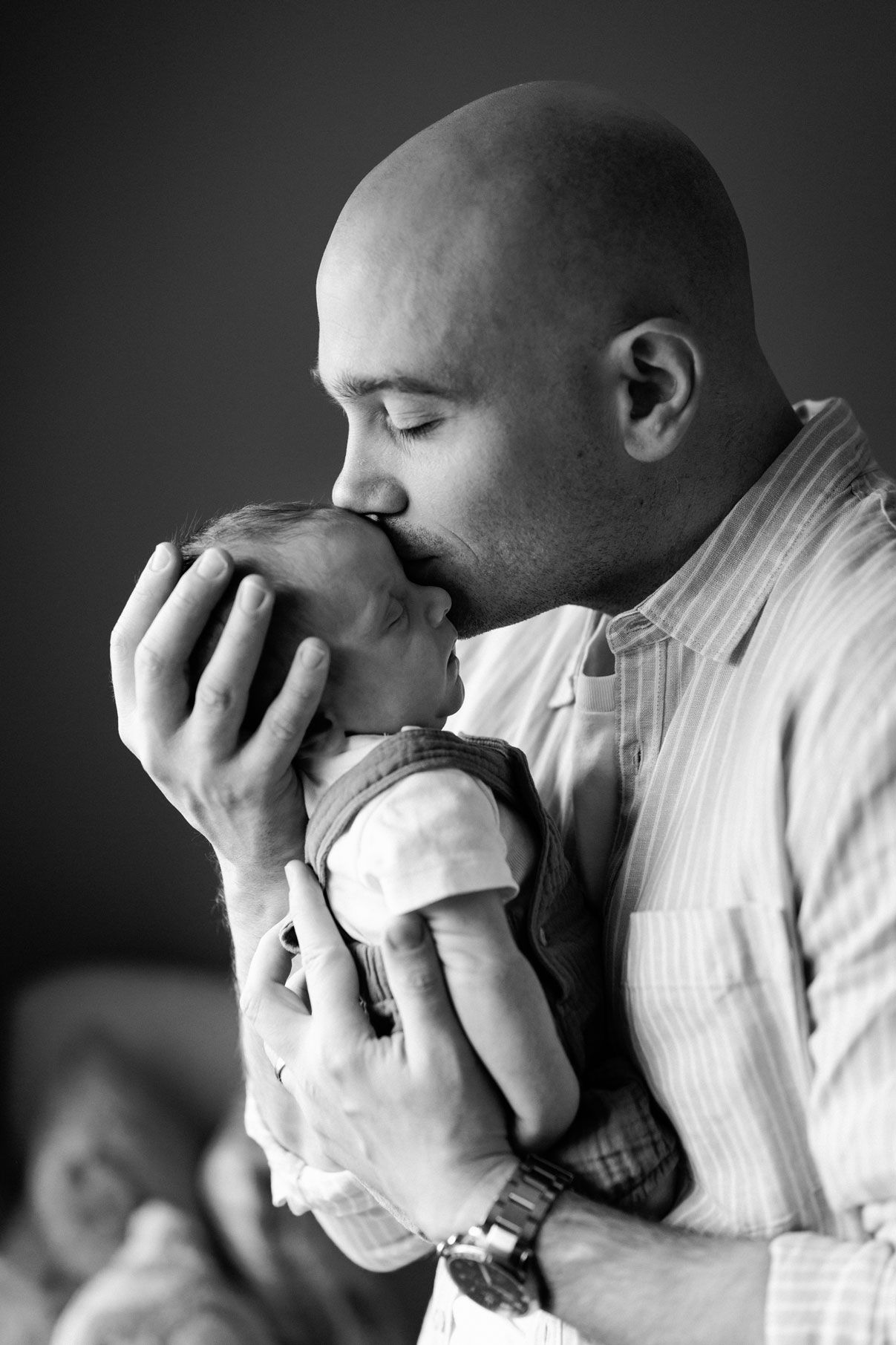 Bald father tenderly kissing his newborn baby while cradling the infant in his hands, black and white photo.