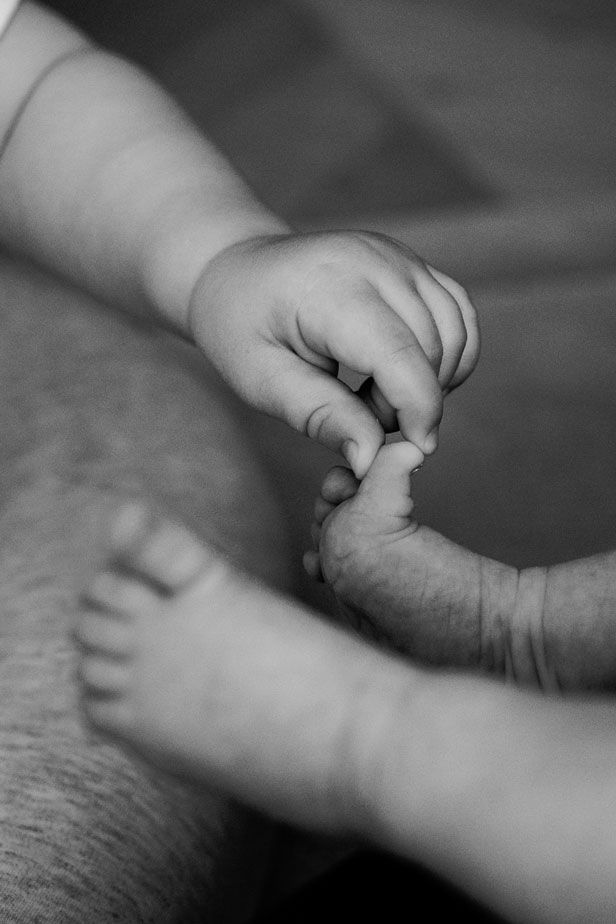 Black and white close-up of a baby's tiny hand and feet, capturing a tender newborn moment.