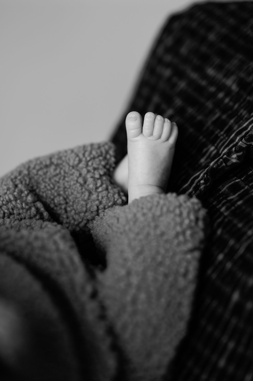 Black and white close-up of a newborn baby's tiny foot peeking out from a soft, fuzzy blanket.