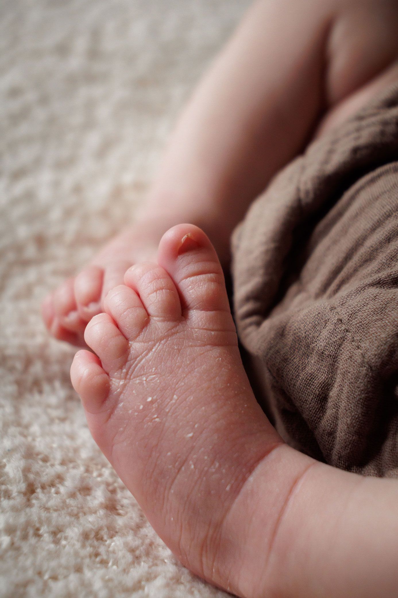 Close-up of tiny newborn baby feet with peeling skin resting on a soft cream blanket in their Nottingham Newborn Session