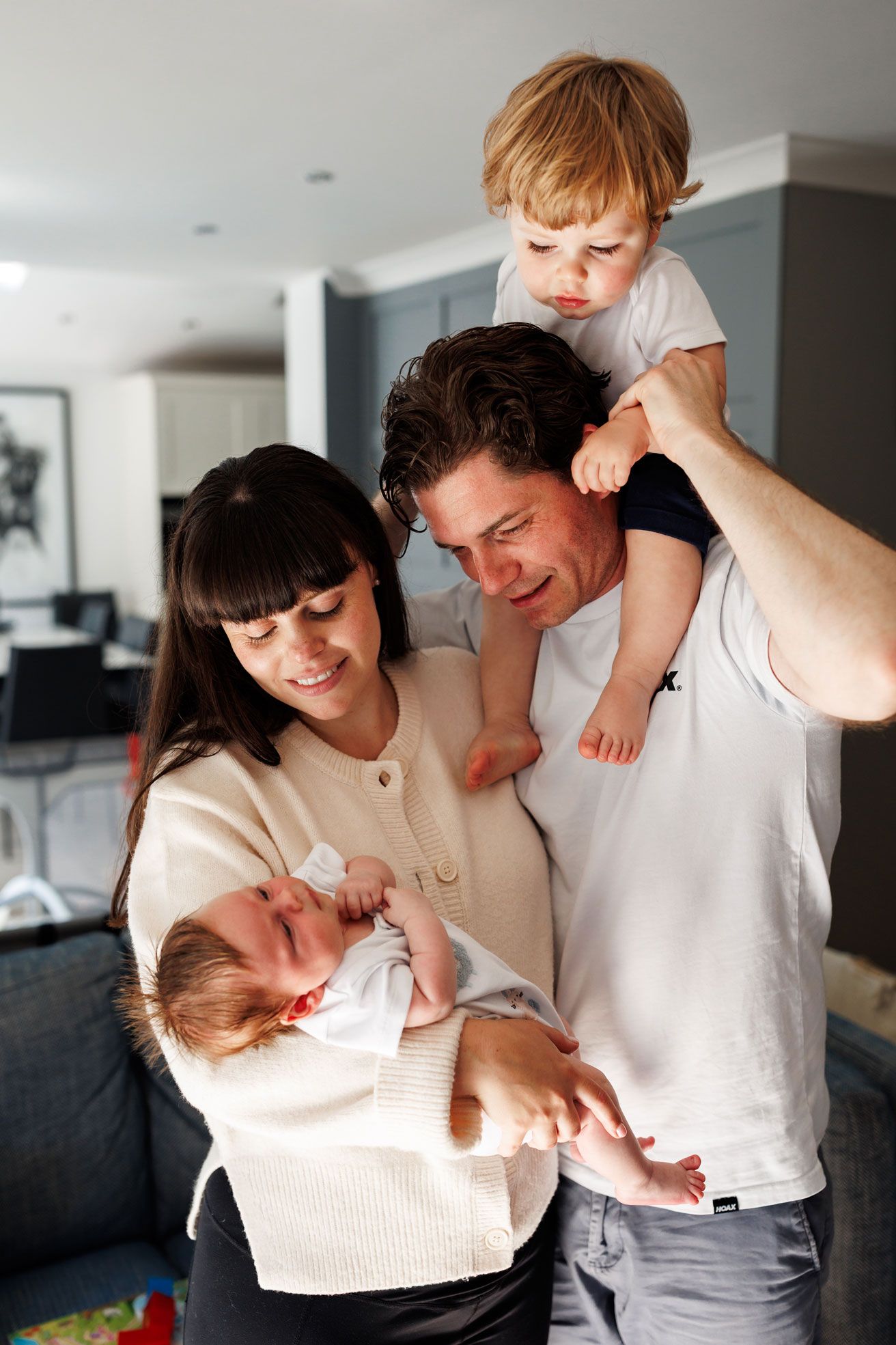 Happy family with mother holding newborn baby and father carrying toddler on shoulders in modern home.
