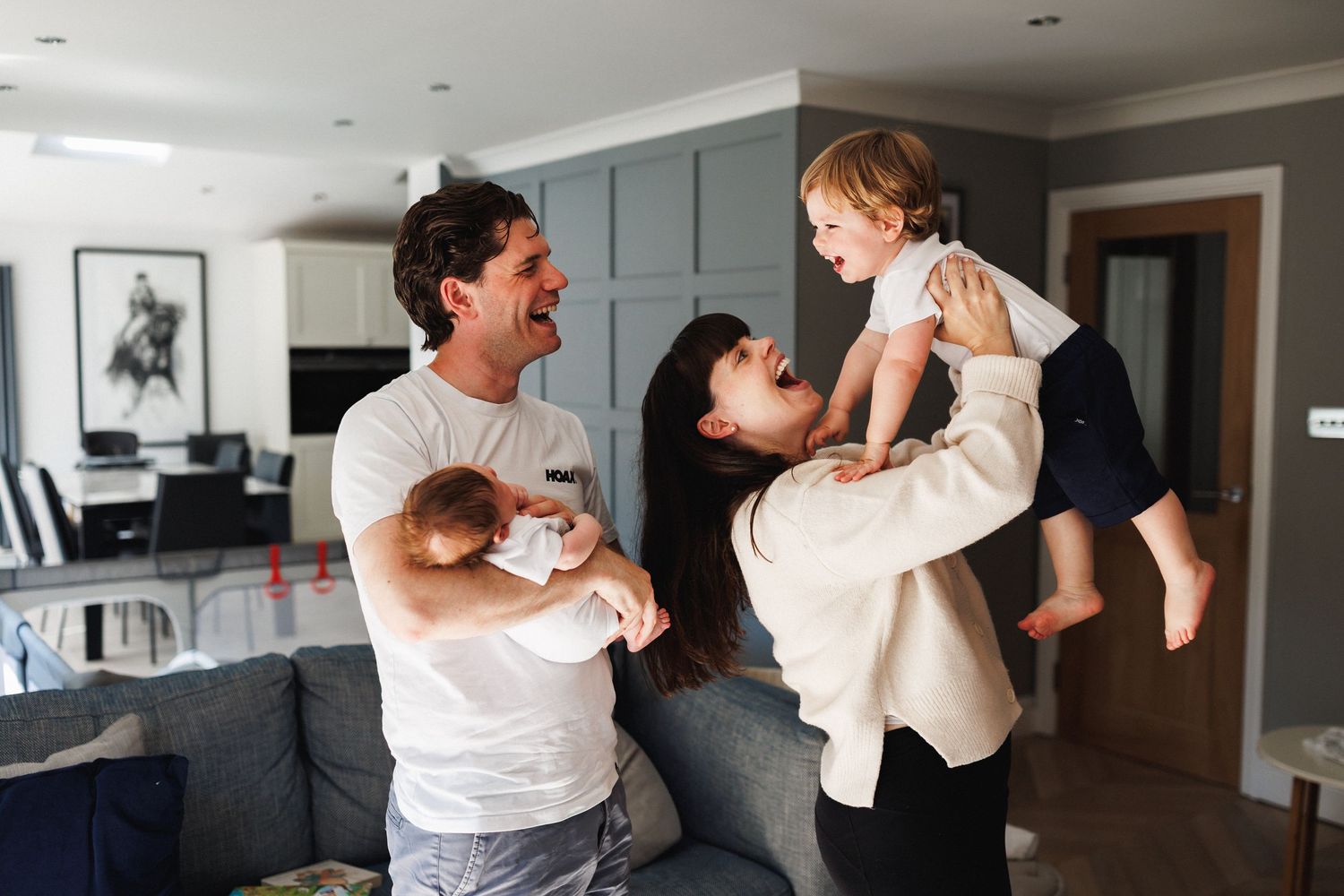 Happy family with two young children laughing and playing together in a modern living room.