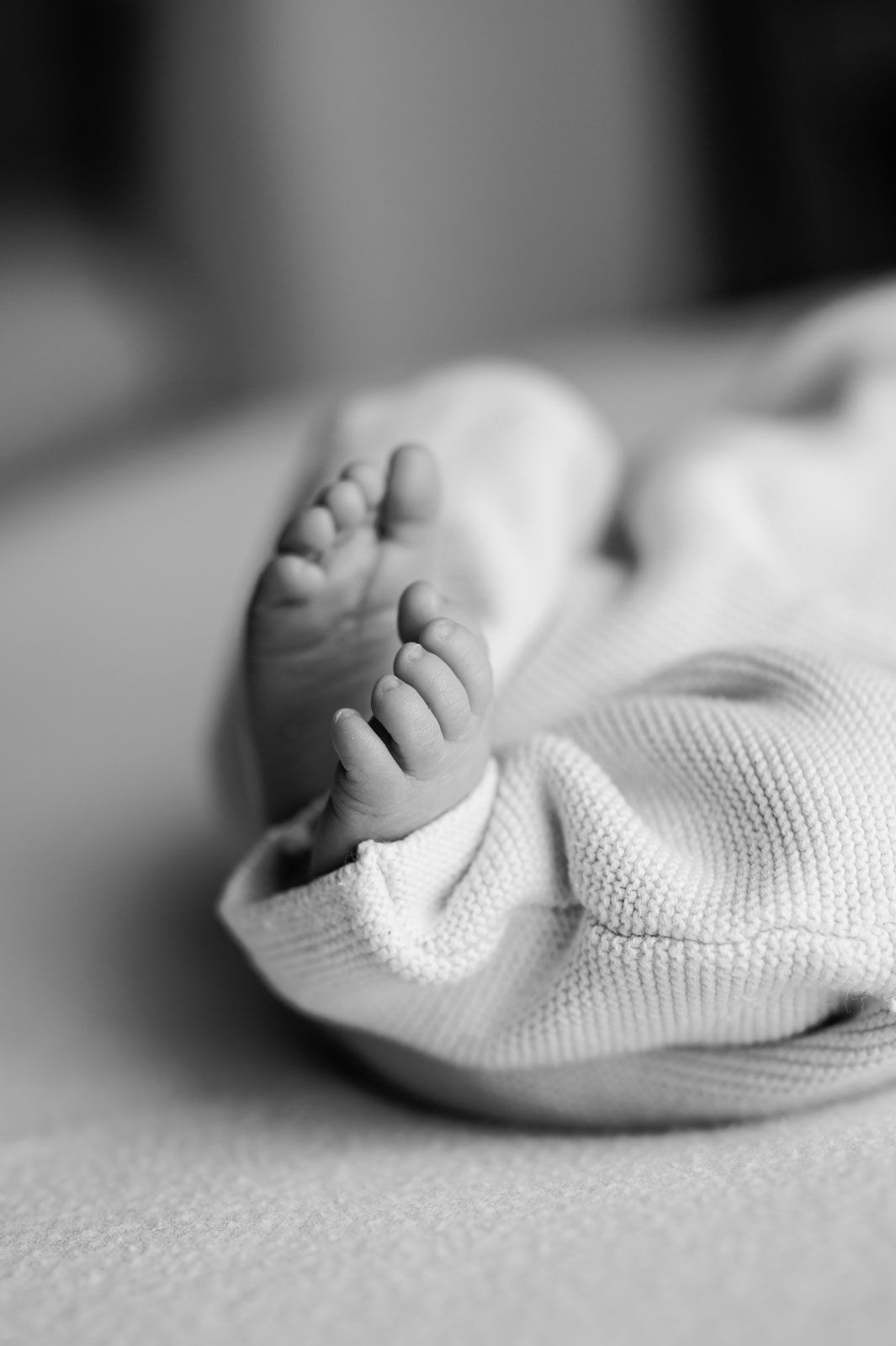 Black and white close-up of a newborn baby's tiny feet peeking out from a soft knit blanket.