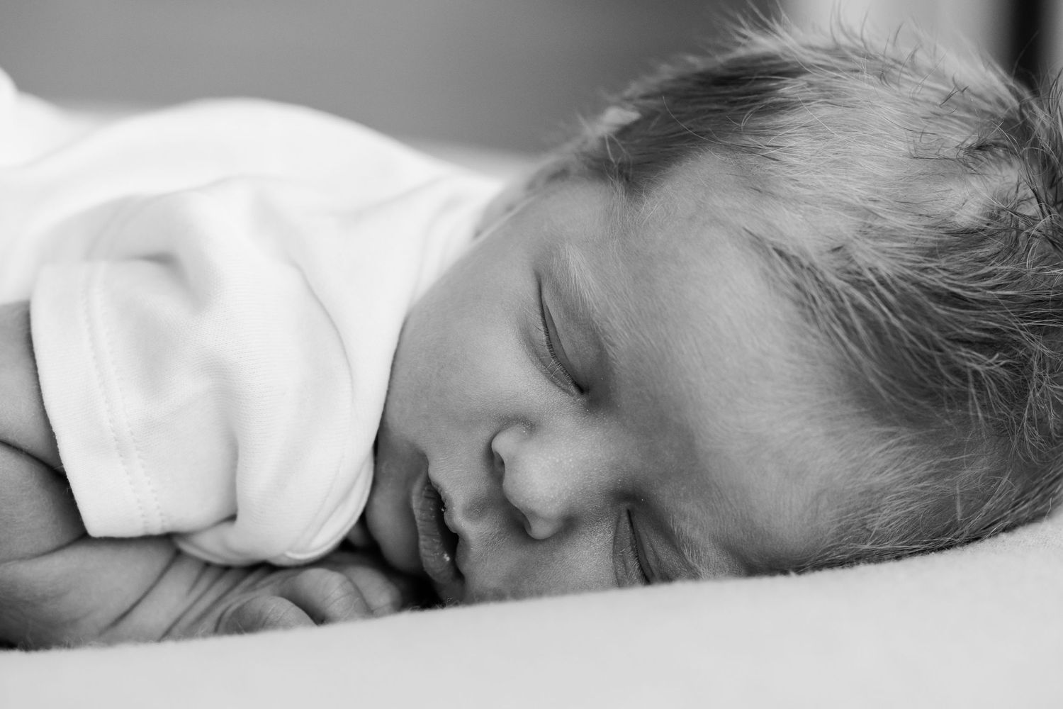 Black and white close-up portrait of a peaceful sleeping newborn baby on a soft surface.