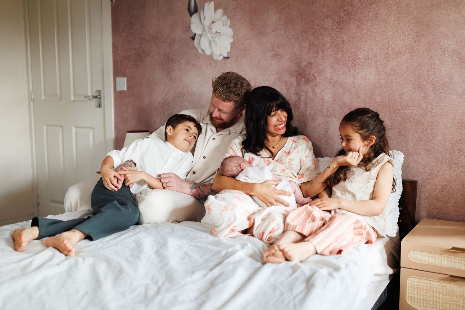 Family of five relaxing together on a bed with their newborn baby at home.