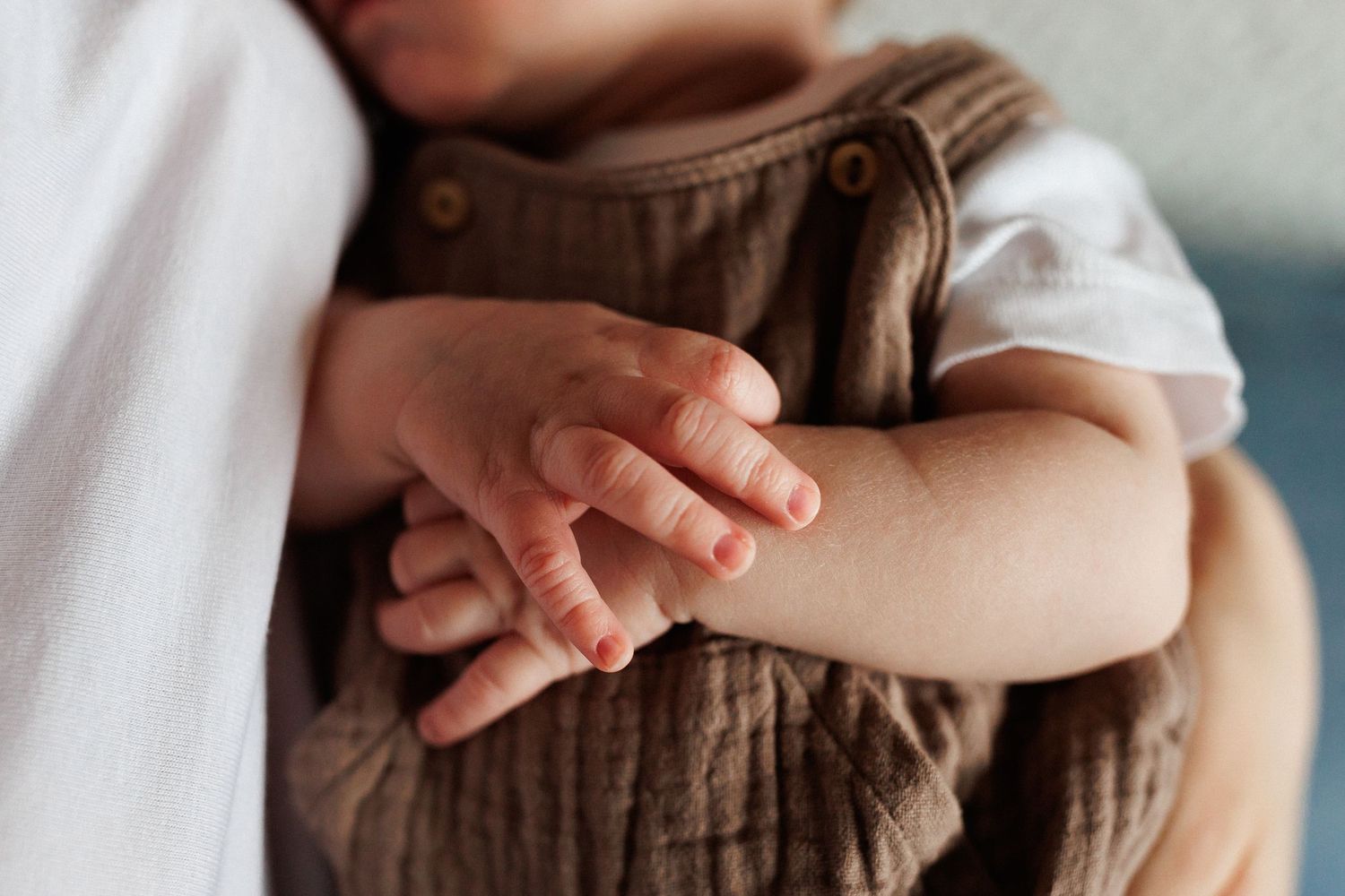 Close-up of a newborn baby's tiny hands resting on brown muslin romper.