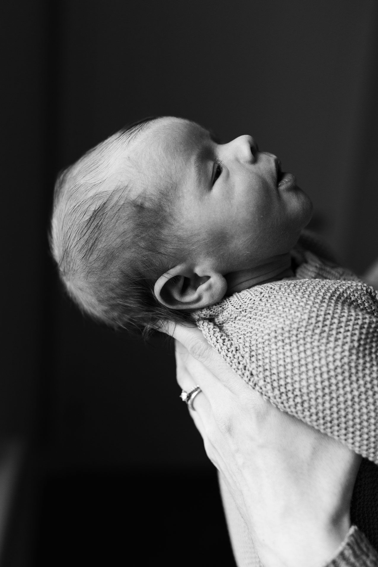 Black and white close-up of a newborn baby being cradled in an adult's hand, head tilted back peacefully.