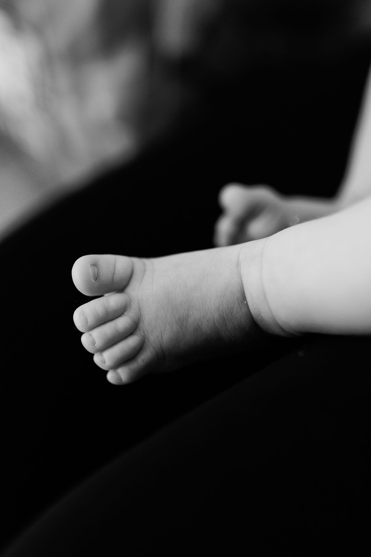 Close-up black and white photo of a newborn baby's tiny foot and toes, capturing delicate details.