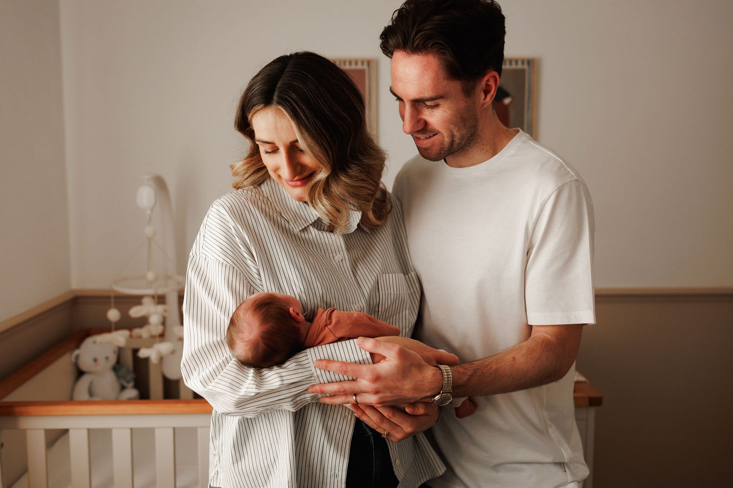 A young couple lovingly holds their newborn baby in a softly lit nursery room.