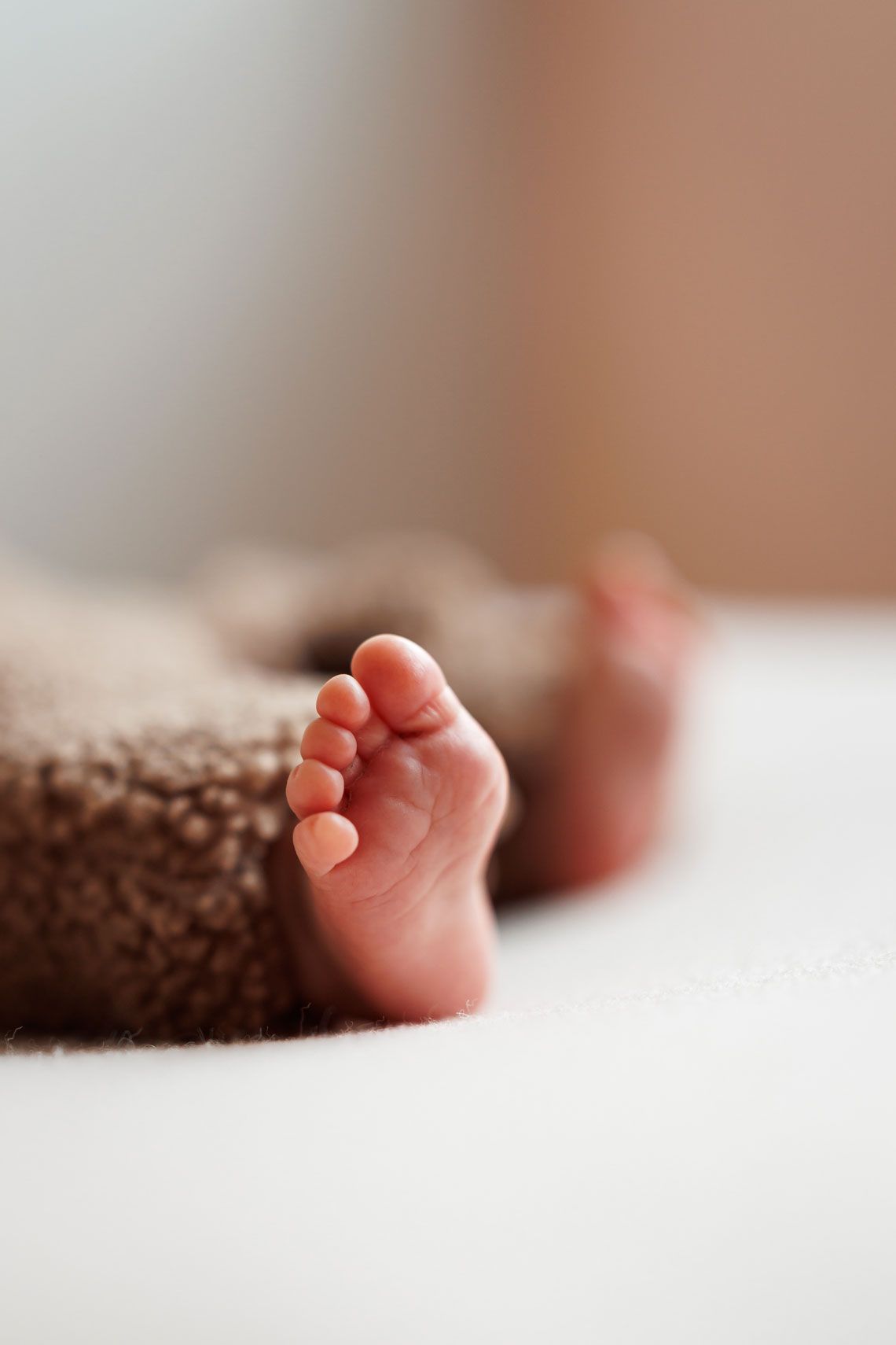 Close-up of a tiny newborn baby foot resting on a soft white blanket next to a cozy brown fleece, with a blurred background.