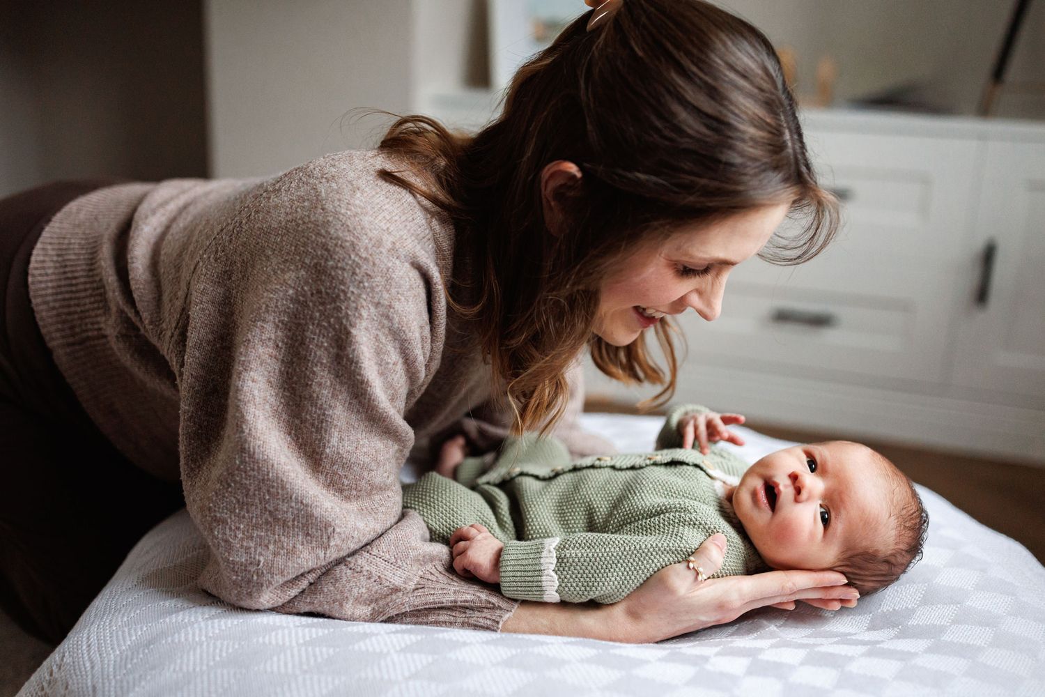 Mother smiling lovingly at her newborn baby lying on white surface.